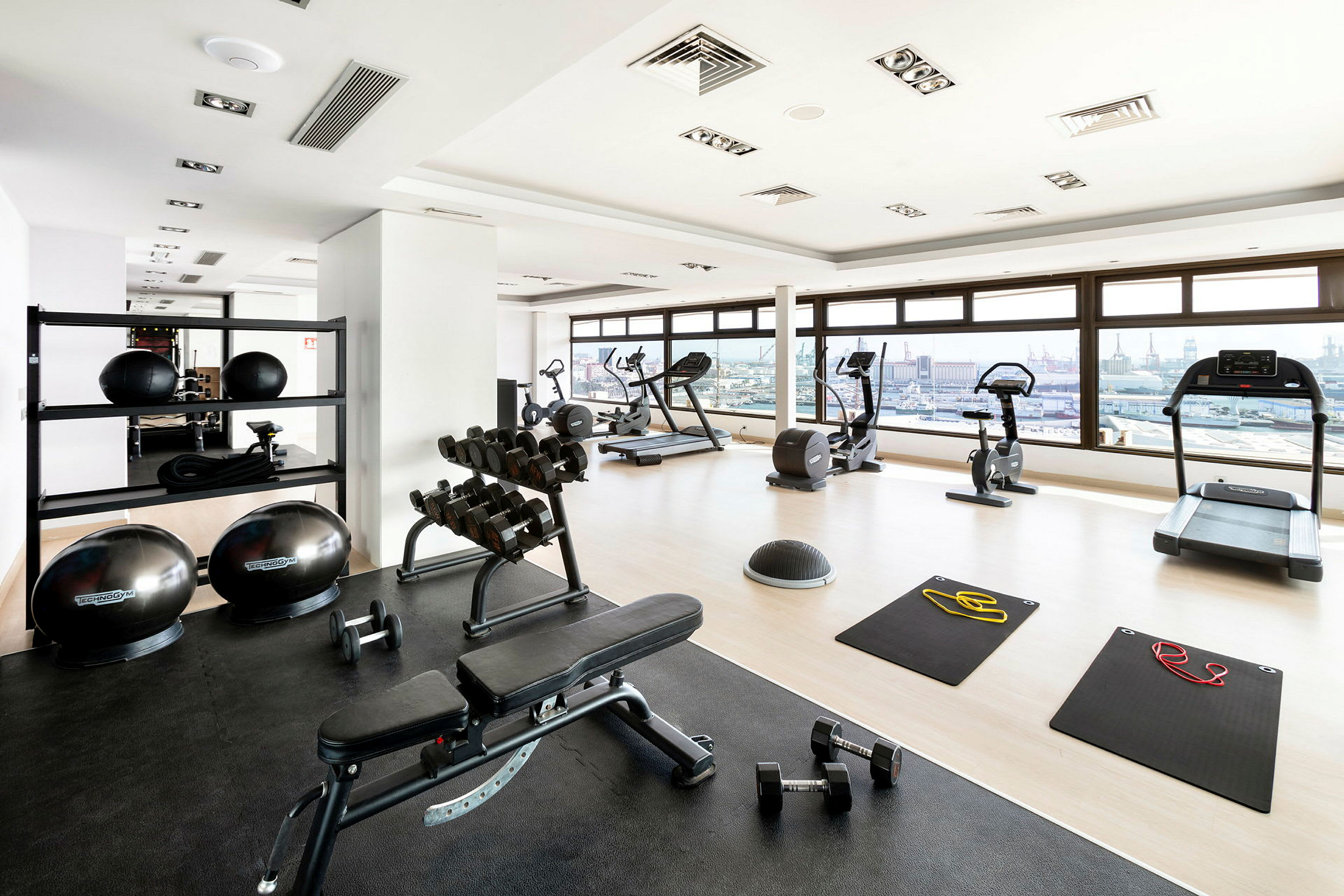 Billede af et fitnesscenter med konditionsmaskiner, bænke, frie vægte og træningsmåtter. (AI-genereret tekst)