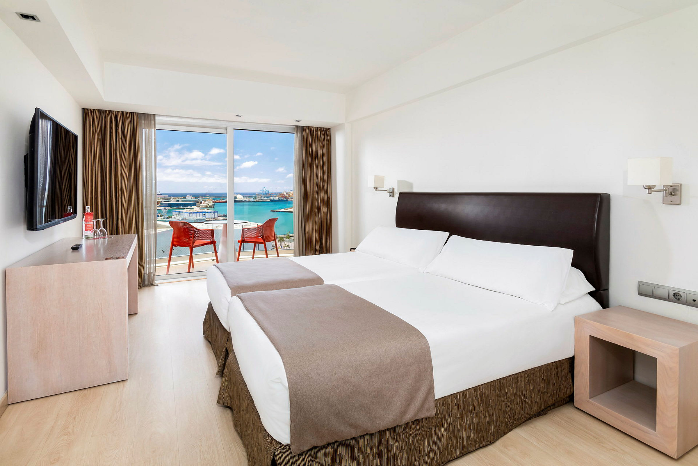 Et hotelværelse med to enkeltsenge og en altan med udsigt over havet. (AI-genereret tekst)