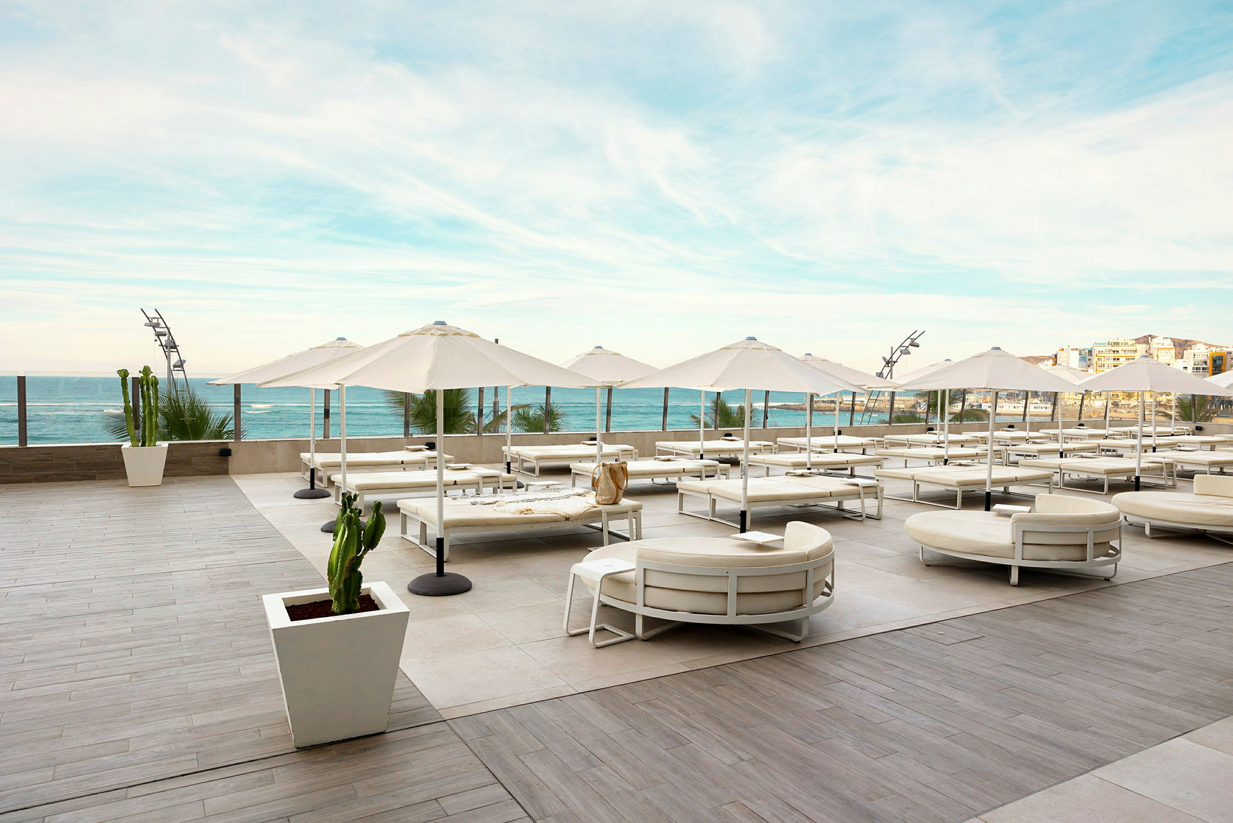 Udendørsområde med liggestole og parasoller på en rummelig terrasse med udsigt over havet. (AI-genereret tekst)