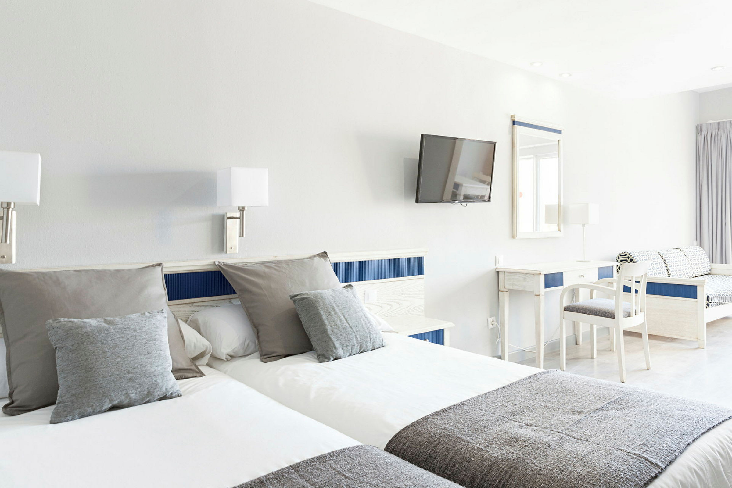 Hotelværelse med to enkeltsenge, skrivebord, stol og vægmonteret tv. (AI-genereret tekst)