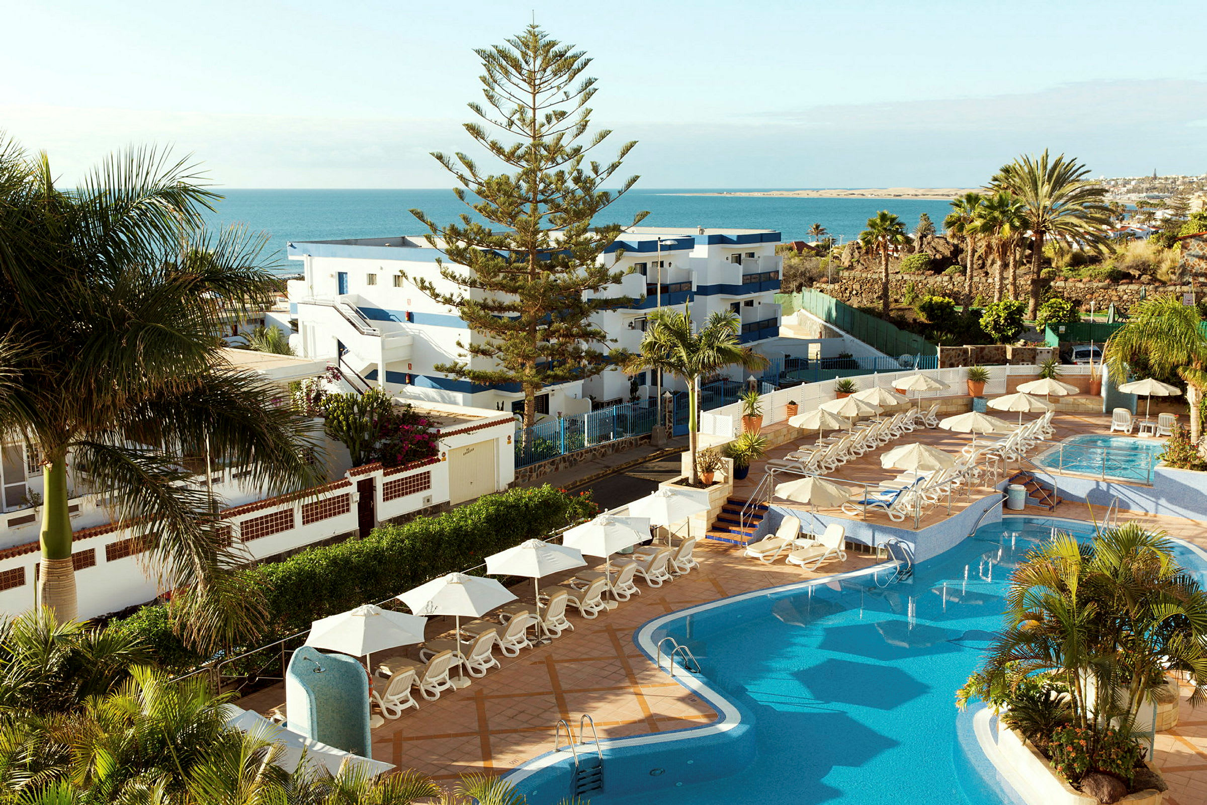 Billede af et hotelområde med pool, liggestole og udsigt over havet. (AI-genereret tekst)
