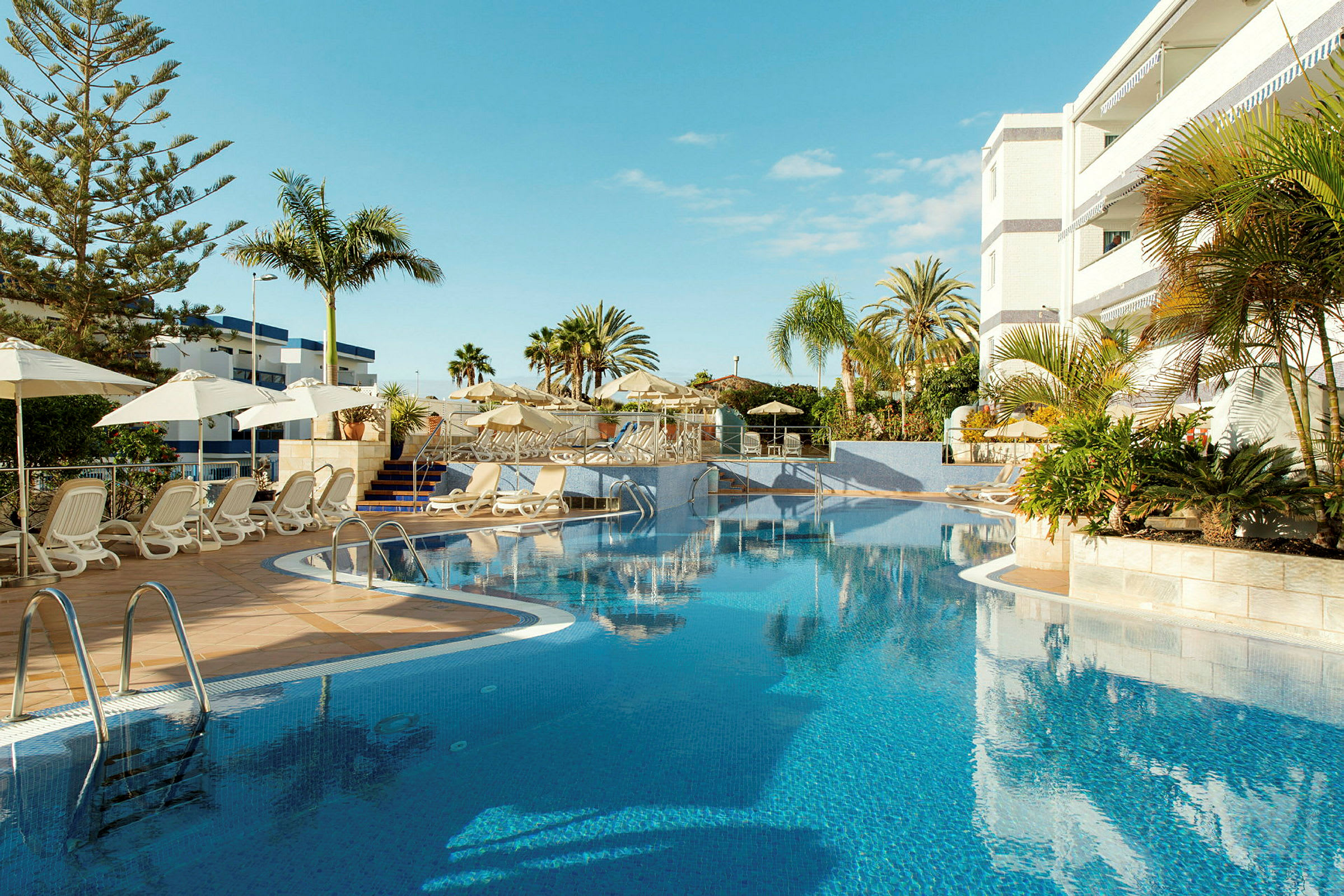 Udendørs pool med liggestole og parasoller ved et hotel. (AI-genereret tekst)
