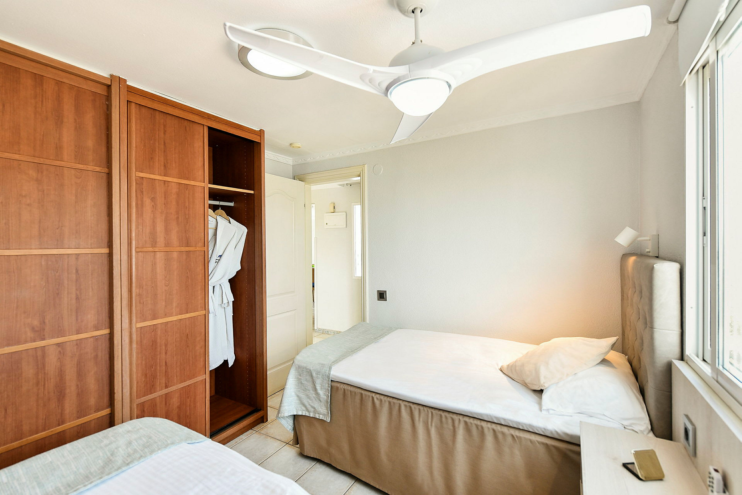 Et hotelværelse med to enkeltsenge, en garderobe med badekåber og en loftventilator. (AI-genereret tekst)