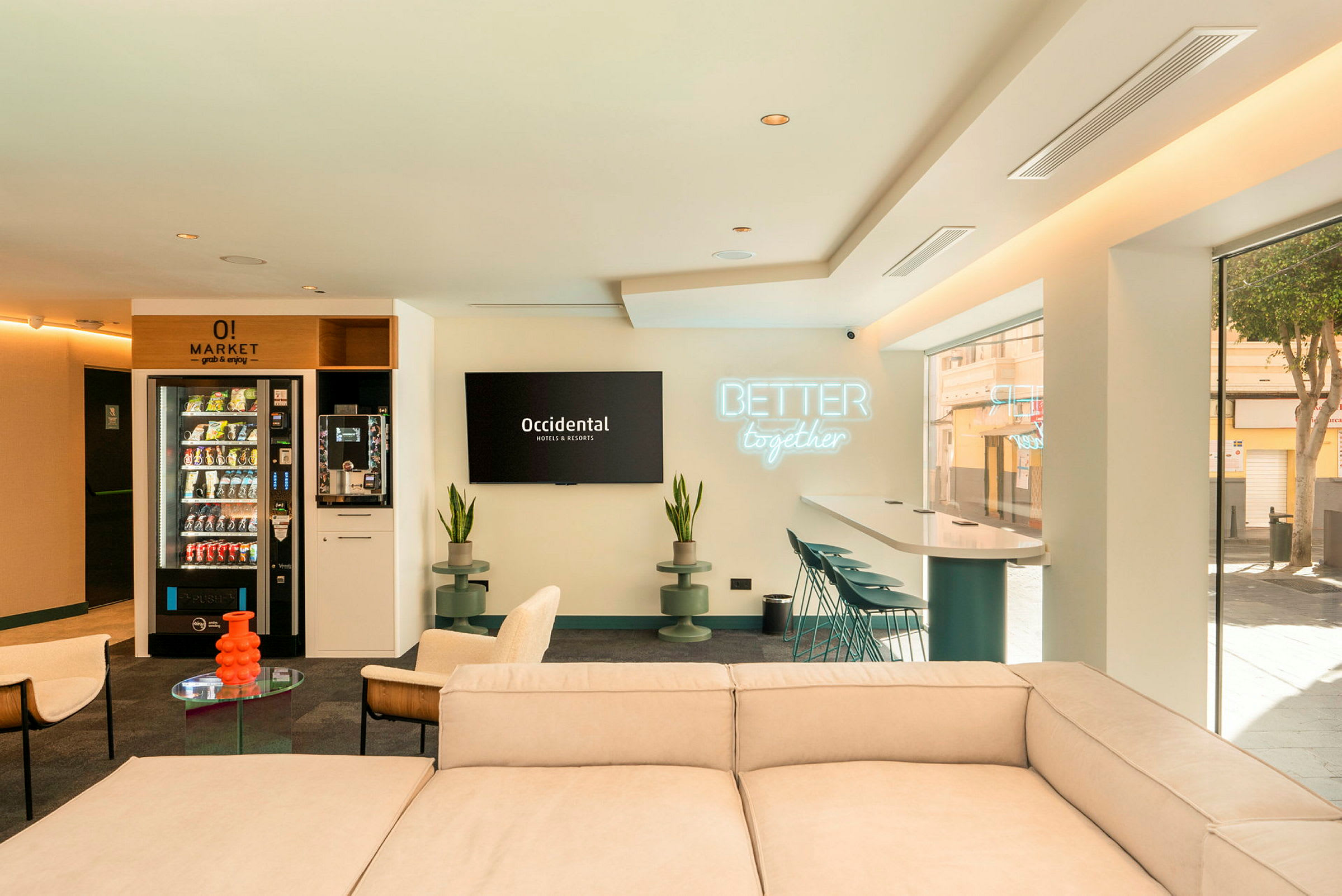 Et moderne og lyst loungeområde med sofa, stole, bord og barstole ved et højt bord. Væggen har en skilt med teksten 'Better together' og en tv med Occidental Hotels & Resorts' logo. (AI-genereret tekst)