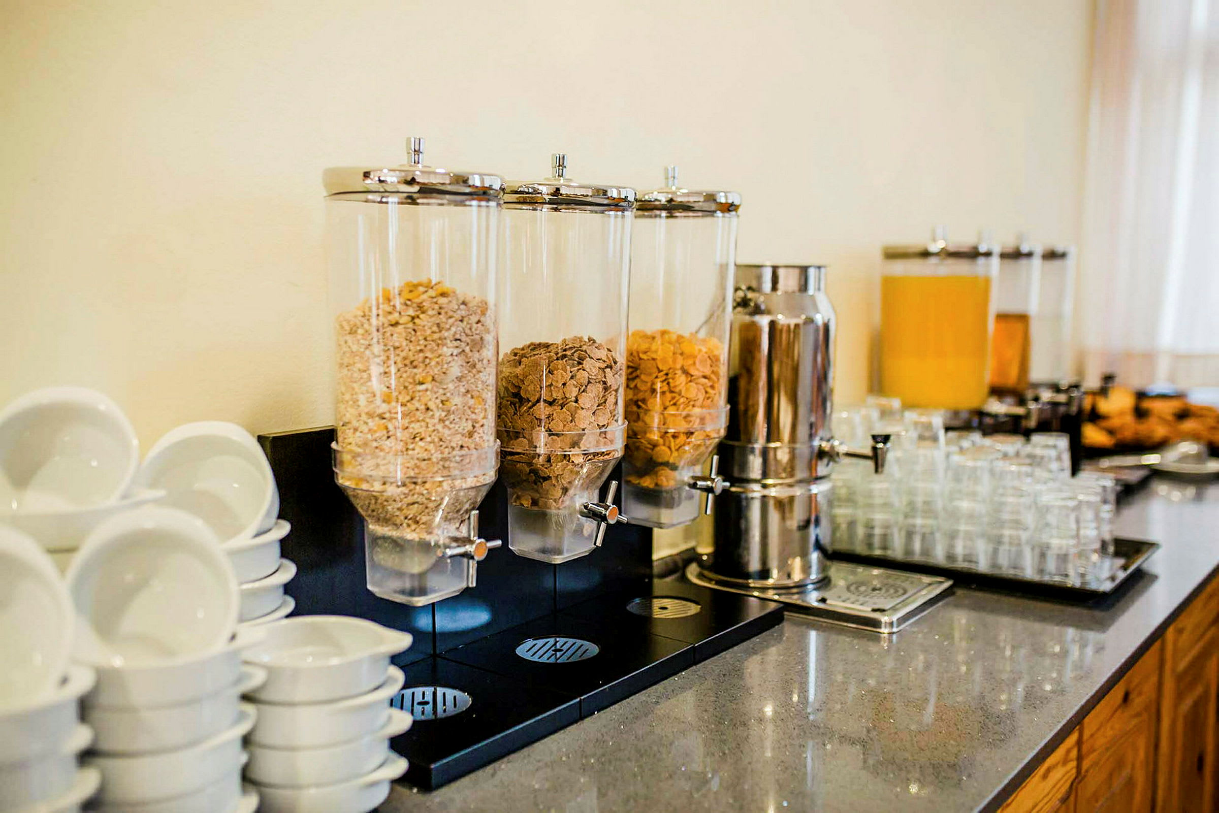 Billede af morgenmadsbuffet med morgenmadsblandingsdispensere, drikkeautomater og kopper. (AI-genereret tekst)