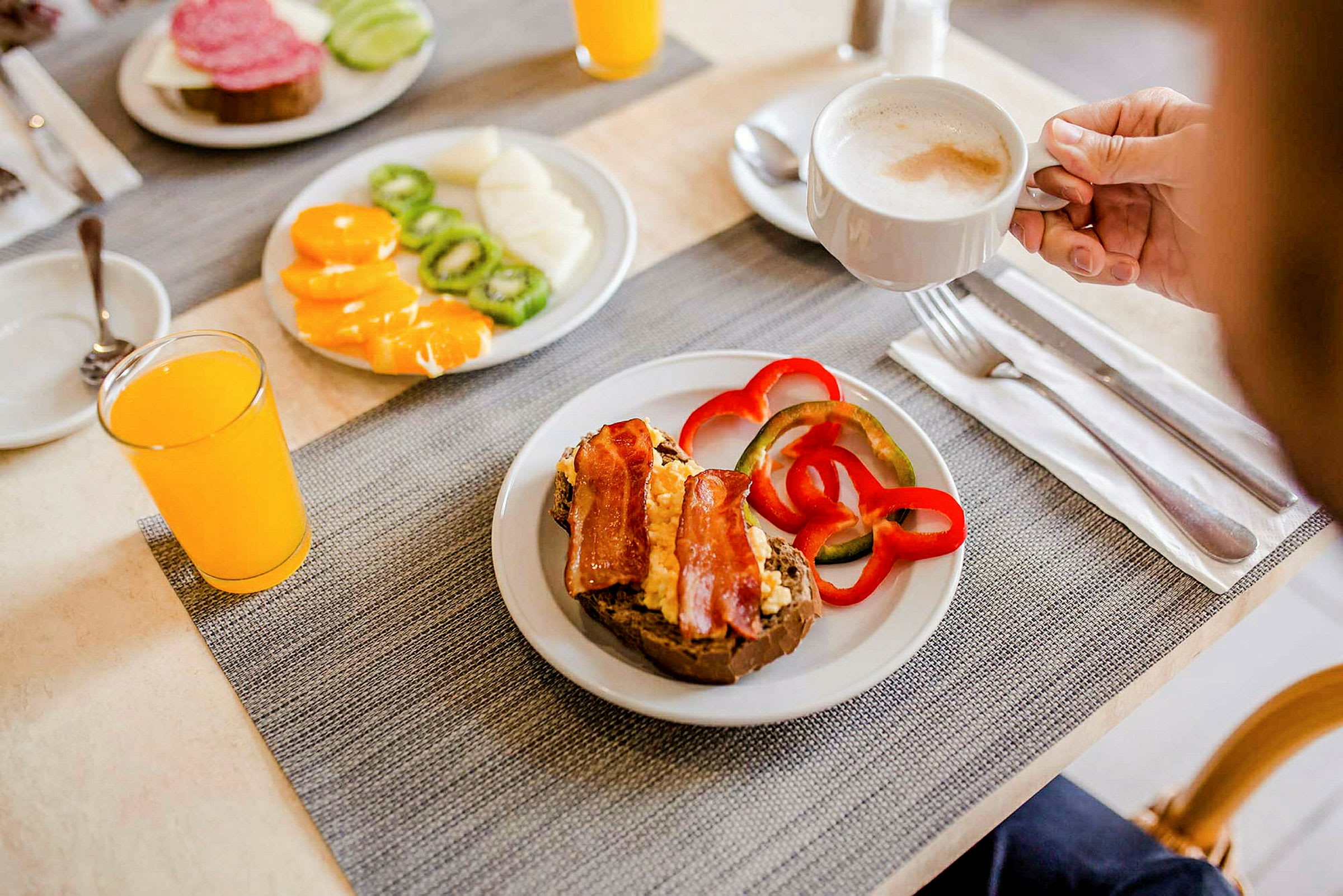 En serveret morgenmad med sandwich, peberfrugt, frugt, appelsinjuice og en kop kaffe. (AI-genereret tekst)