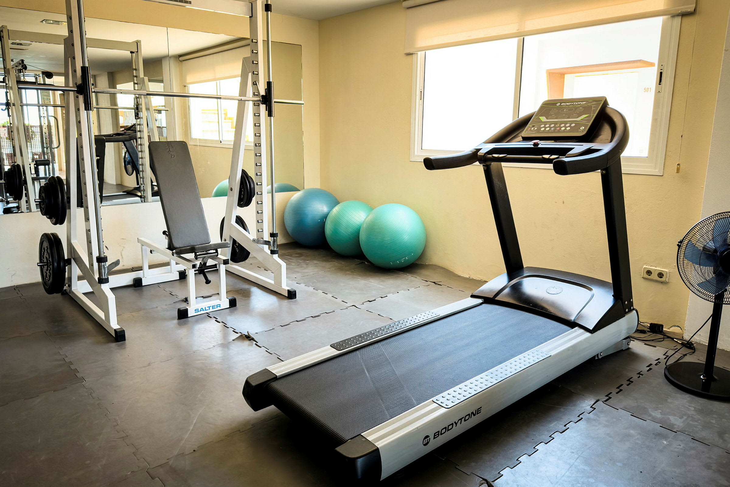 Et fitnessrum med løbebånd, træningsbænk og fitnessbolde. (AI-genereret tekst)
