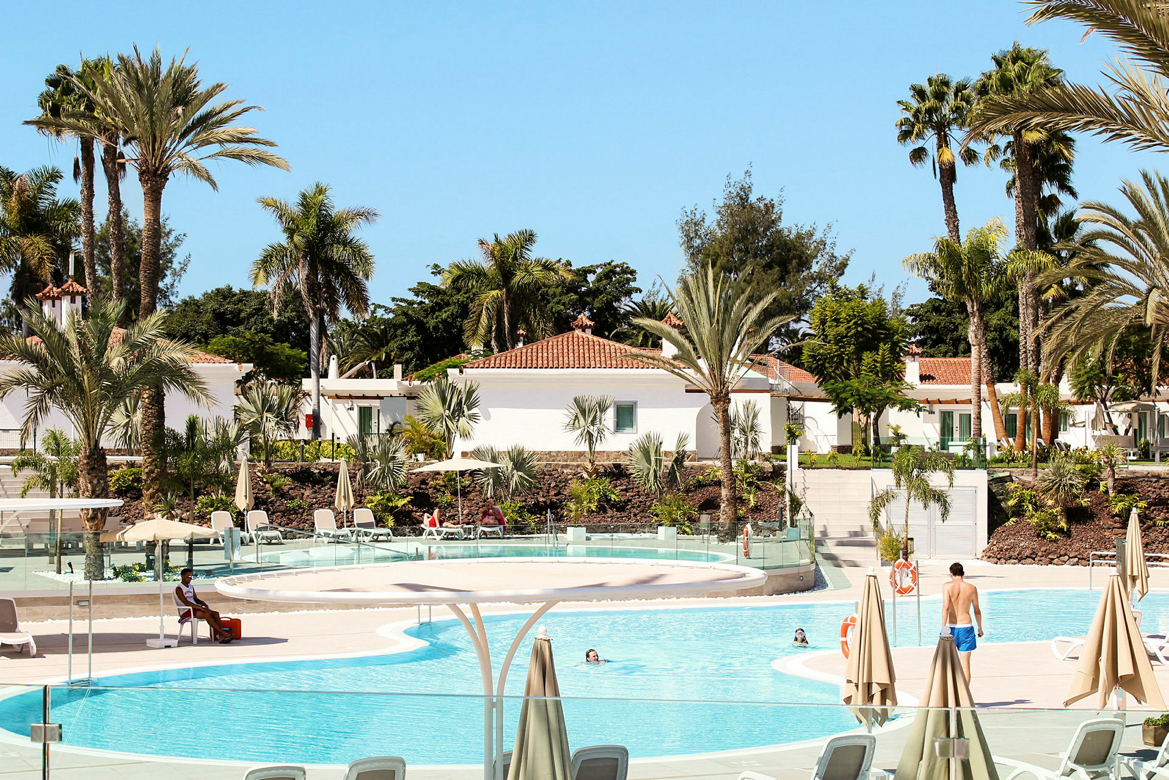 En solrig resort med pool, palmer og hvide bygninger. (AI-genereret tekst)