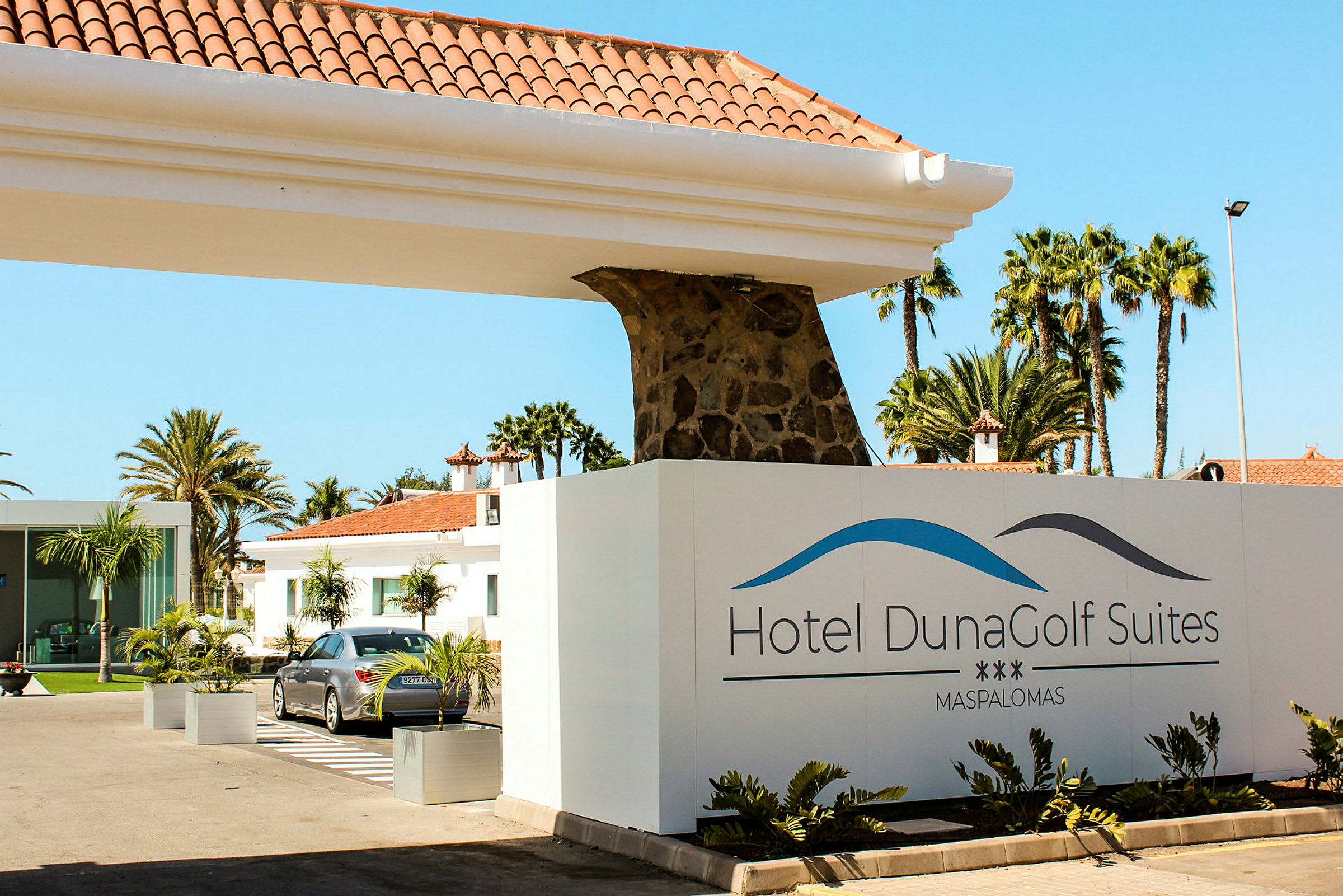 Indgangen til Hotel DunaGolf Suites med skilt og bygninger i baggrunden. (AI-genereret tekst)