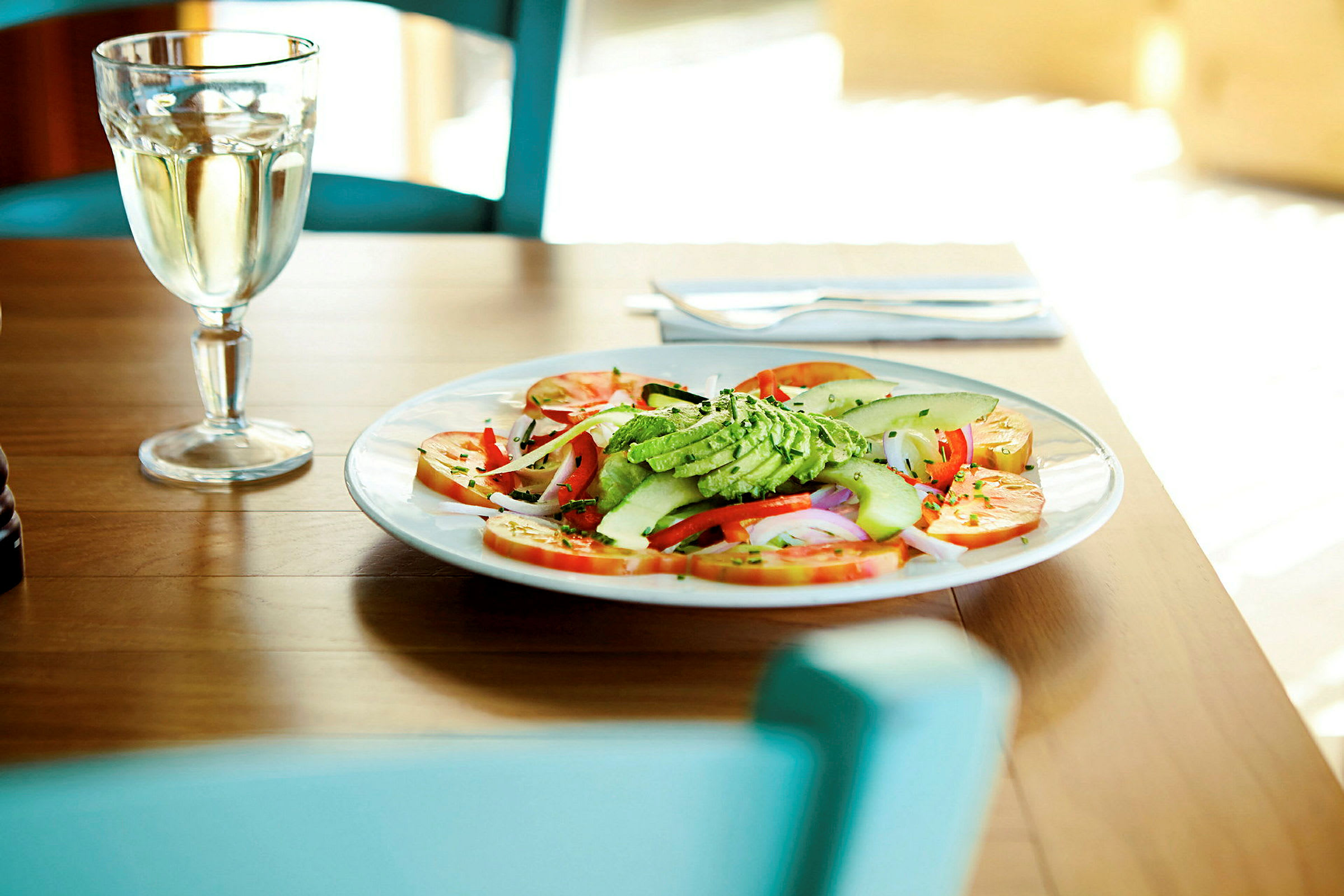 En tallerken med grøntsager og avocado på et bord, ved siden af et glas med drikke. (AI-genereret tekst)