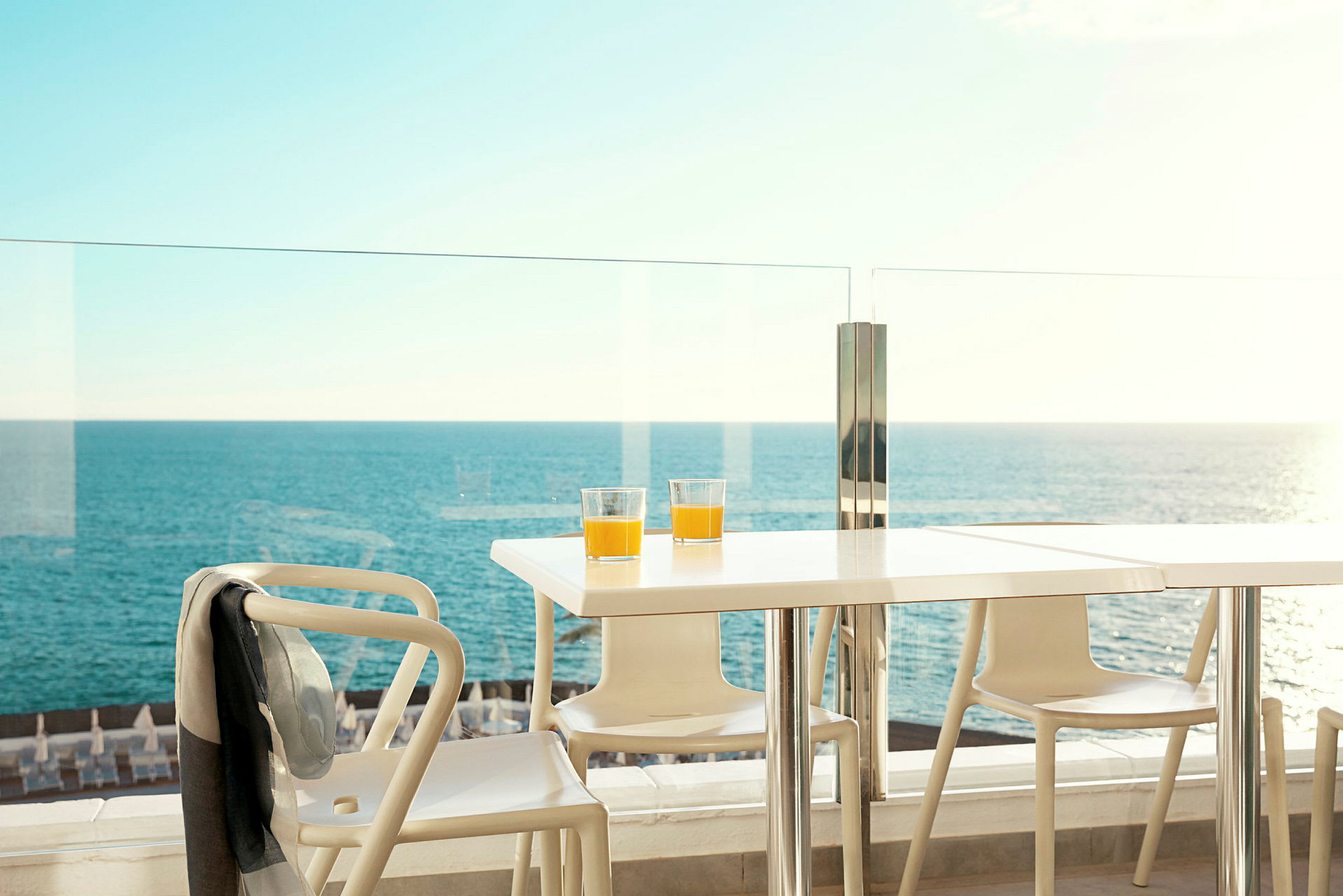 Bord med to glas appelsinjuice på en terrasse med udsigt over havet. (AI-genereret tekst)