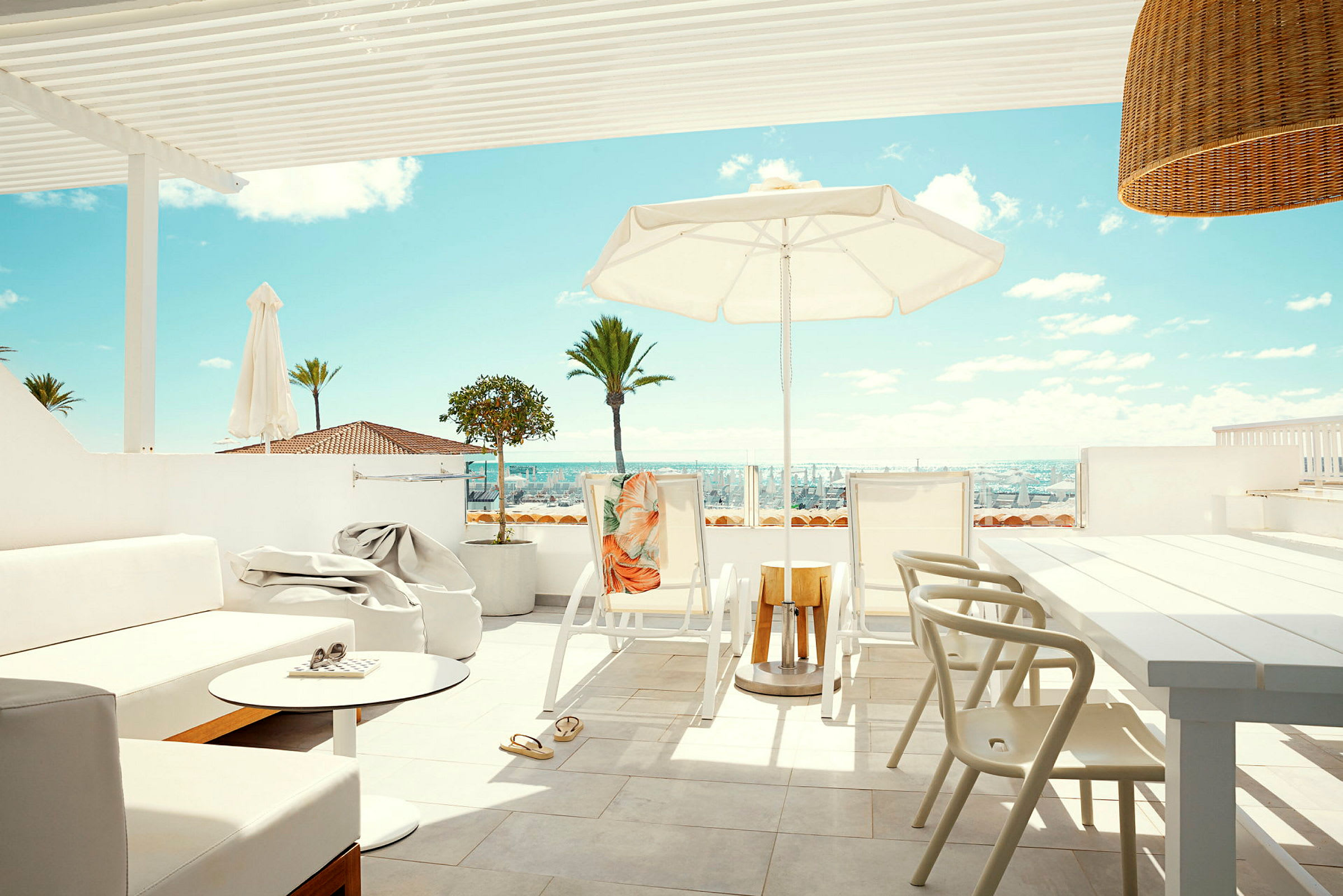 En solrig terrasse med møbler, parasol og udsigt over palmer og havet. (AI-genereret tekst)