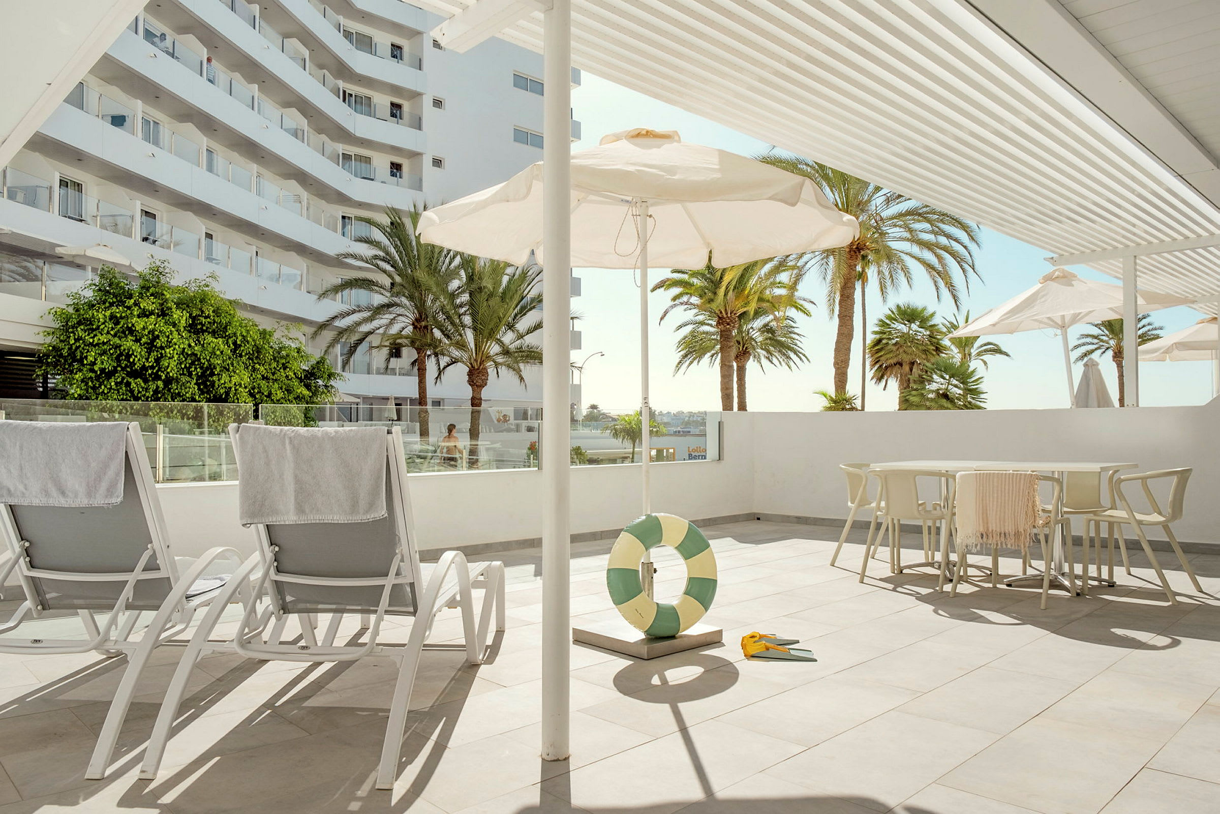Liggestole på en solrig terrasse med parasoller og palmer i baggrunden. (AI-genereret tekst)