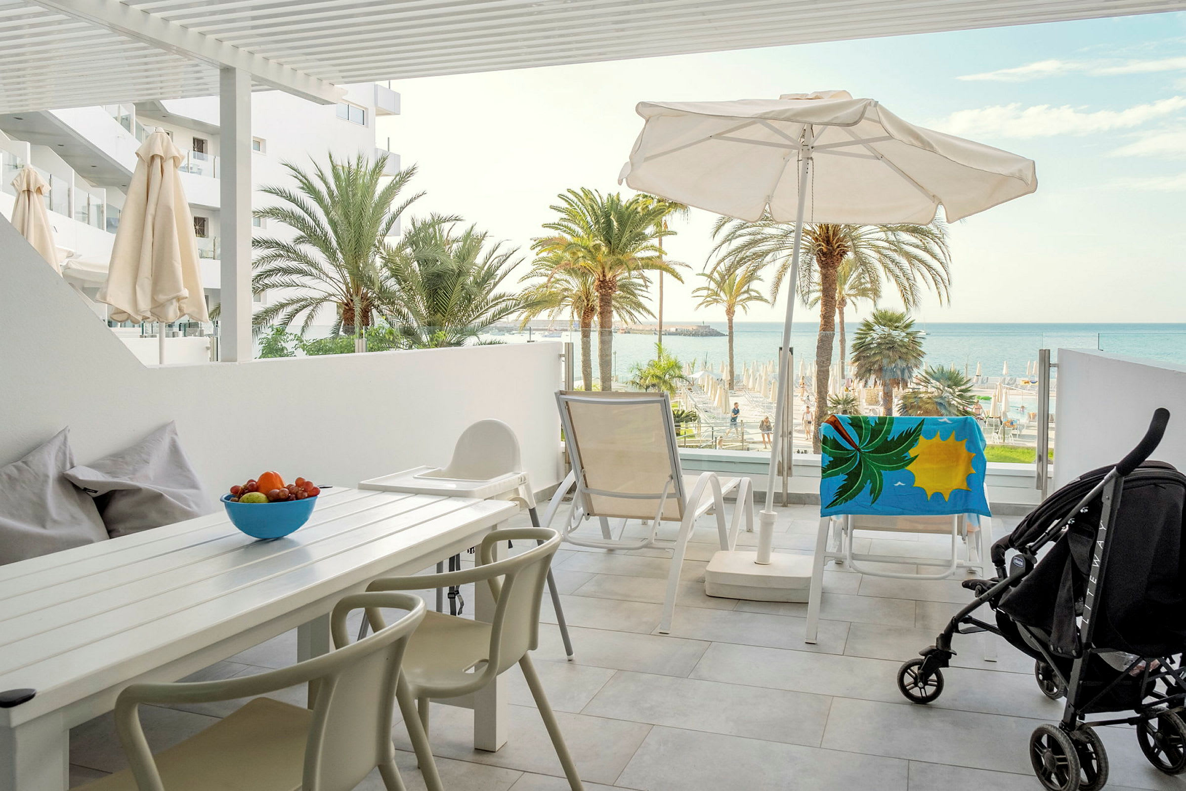 Udsigt fra en møbleret terrasse mod havet og palmer. (AI-genereret tekst)