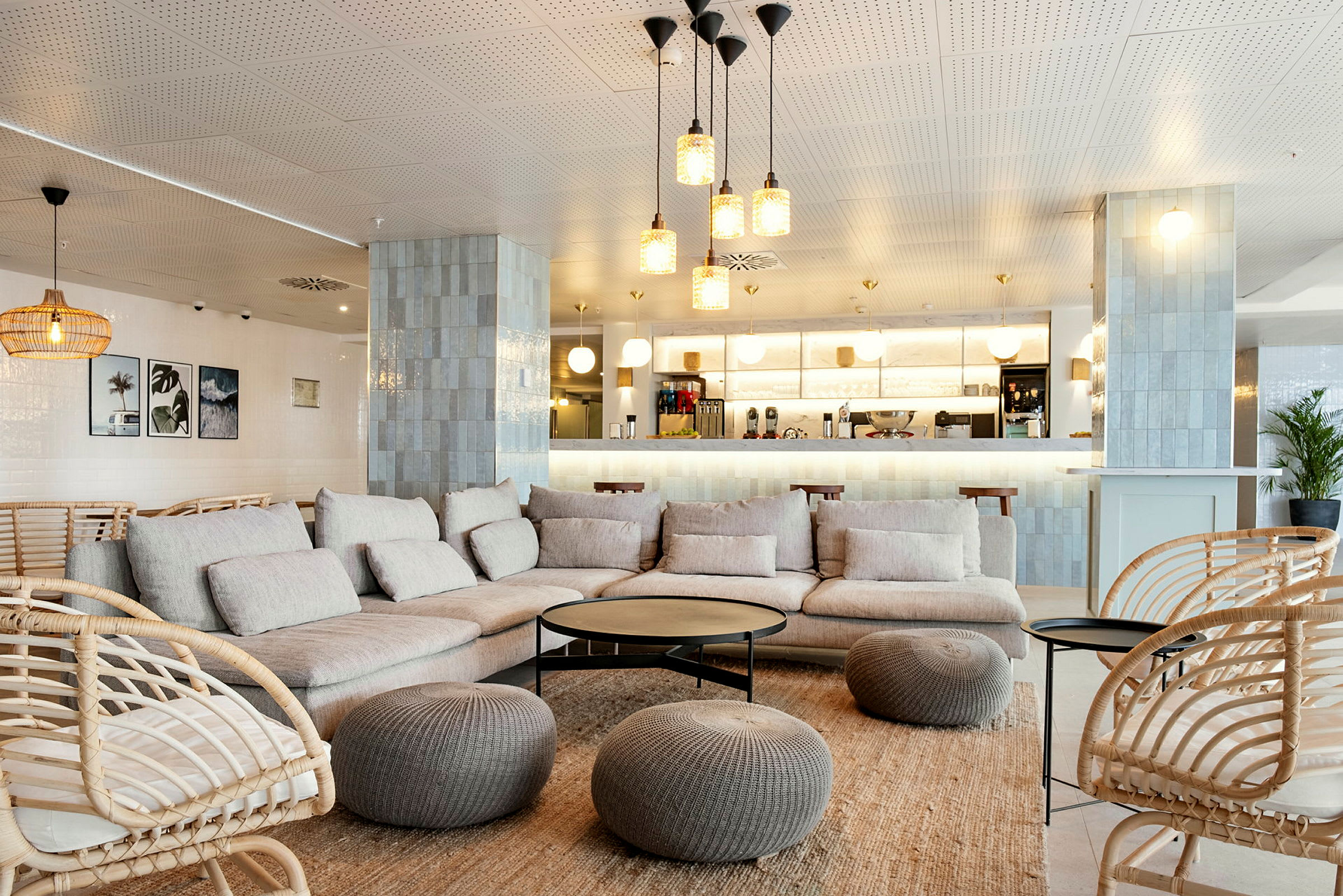 En moderne lounge med beige sofaer og kurvestole, indrettet med borde og dekorationer samt en kaffebar i baggrunden. (AI-genereret tekst)
