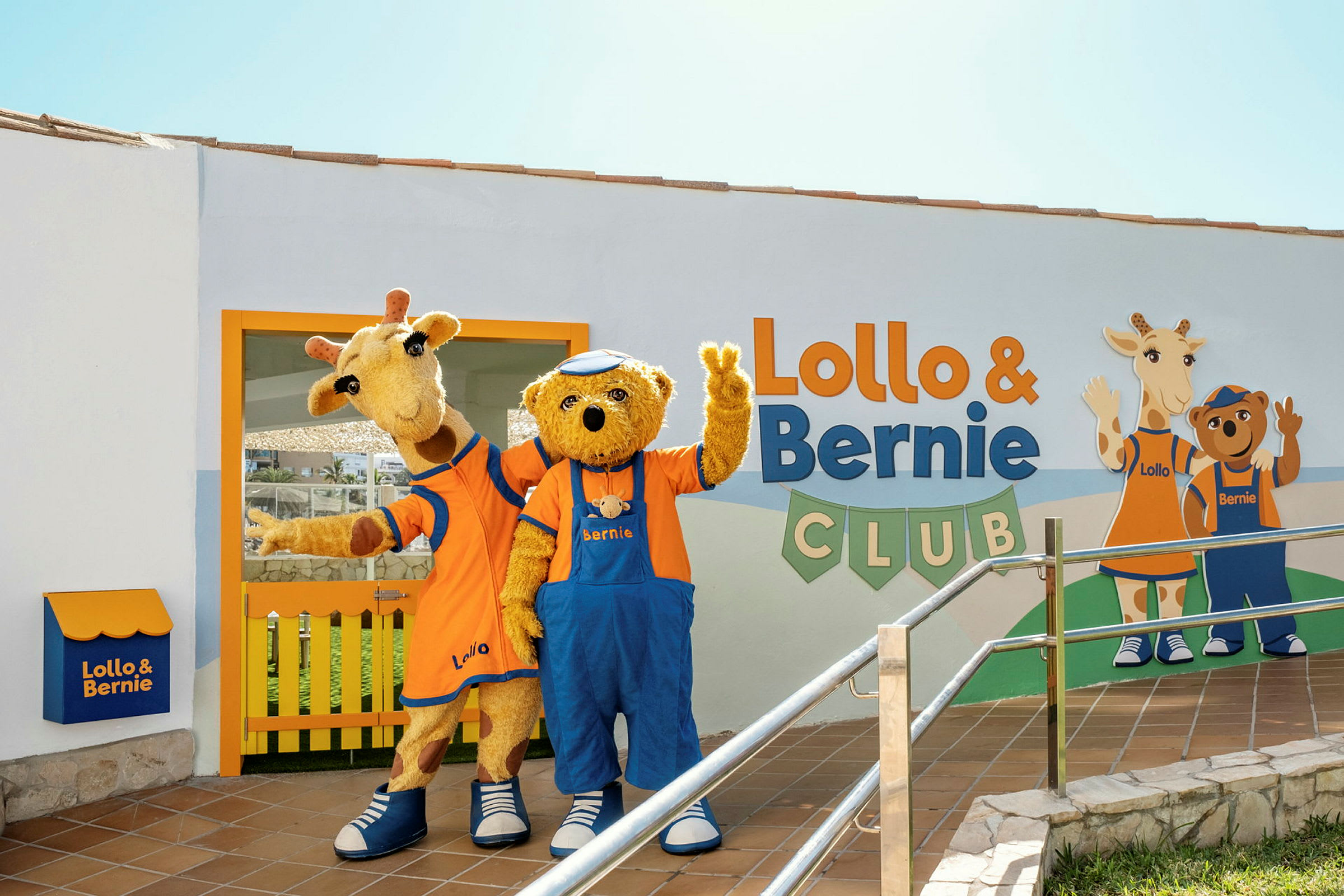 To maskotter, en giraf og en bjørn, står foran Lollo & Bernie Club-bygningen og vinker. (AI-genereret tekst)