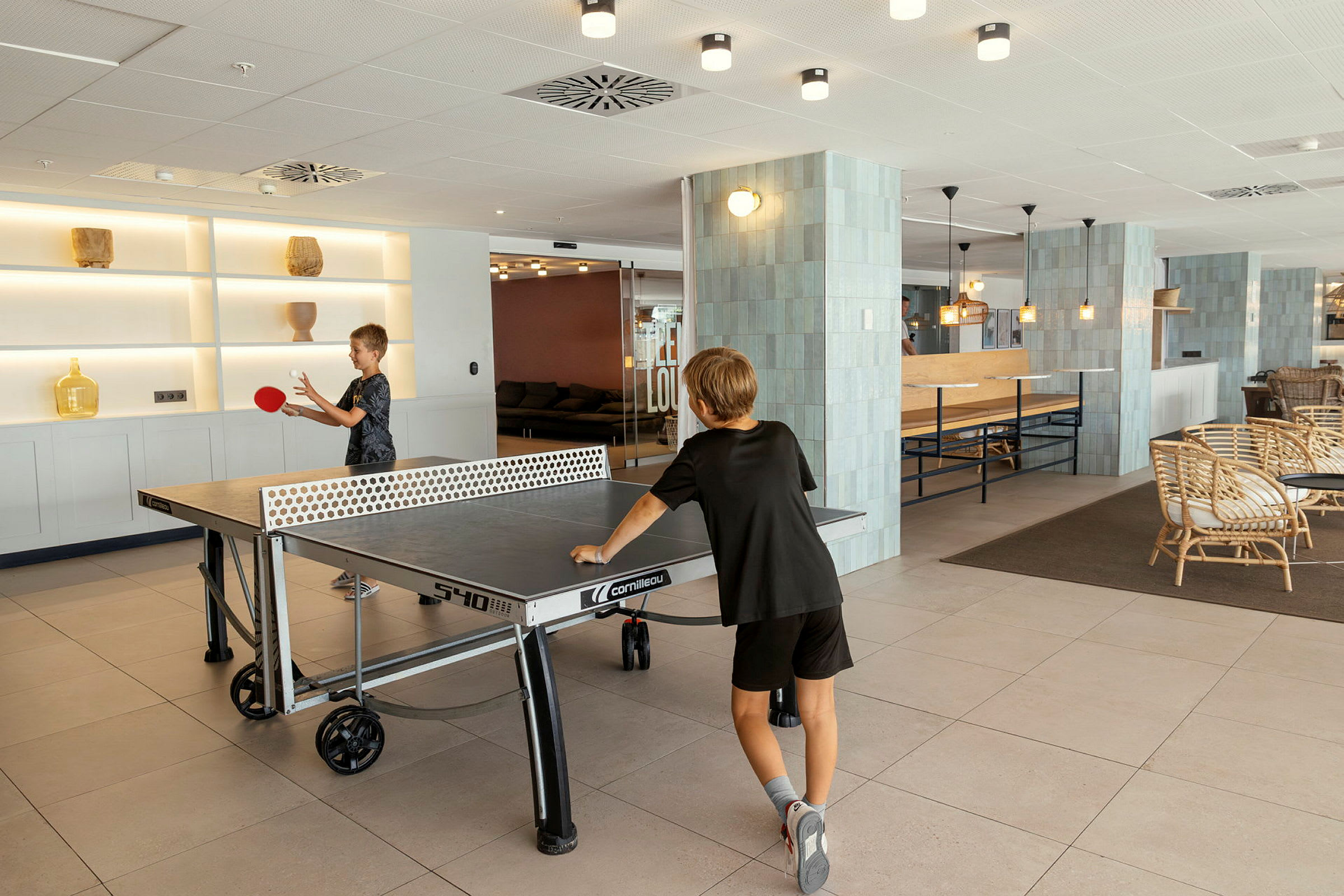 To personer spiller bordtennis i et lyst indrettet fællesområde. (AI-genereret tekst)