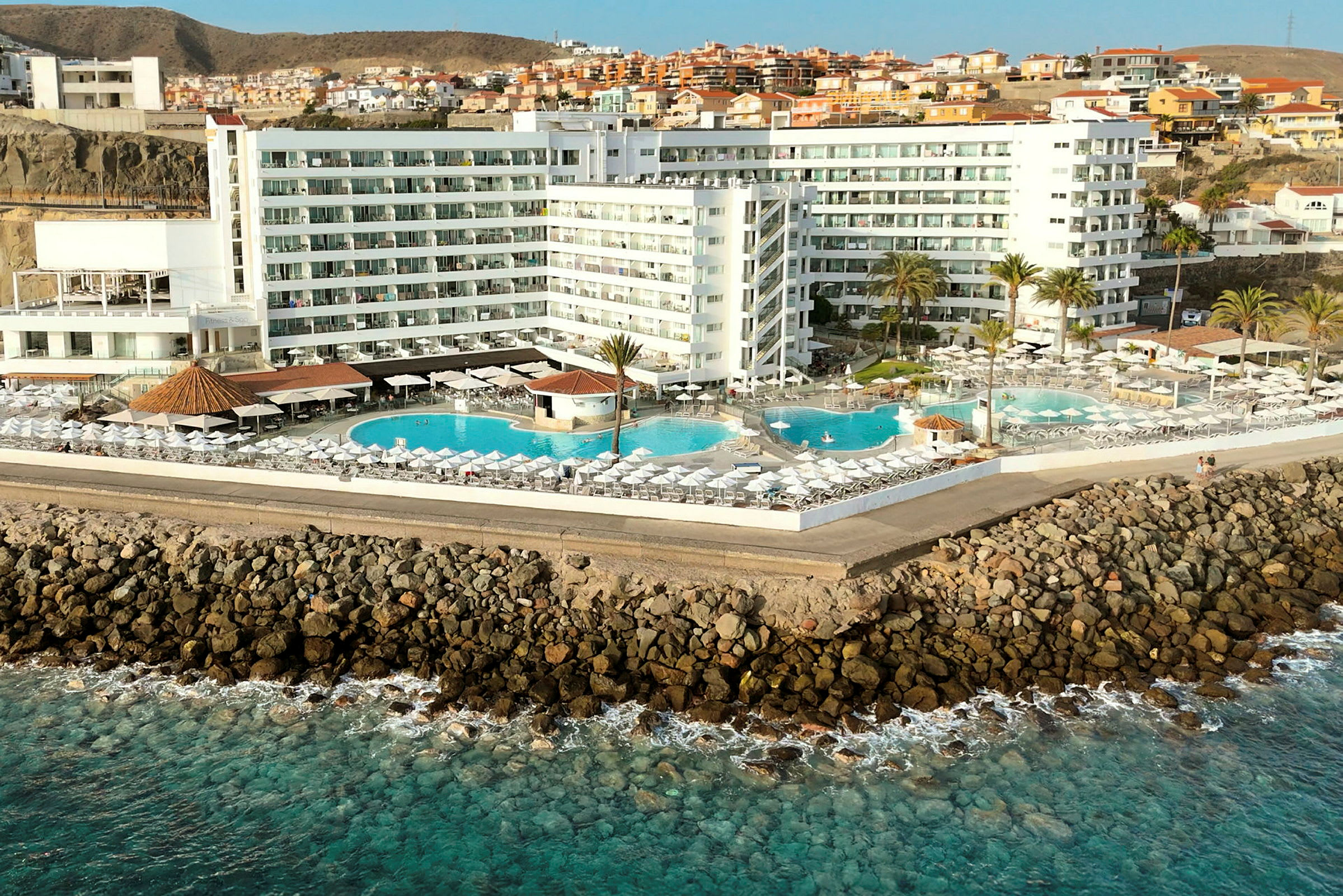 Hotel ved kysten med flere pools og liggestole. (AI-genereret tekst)