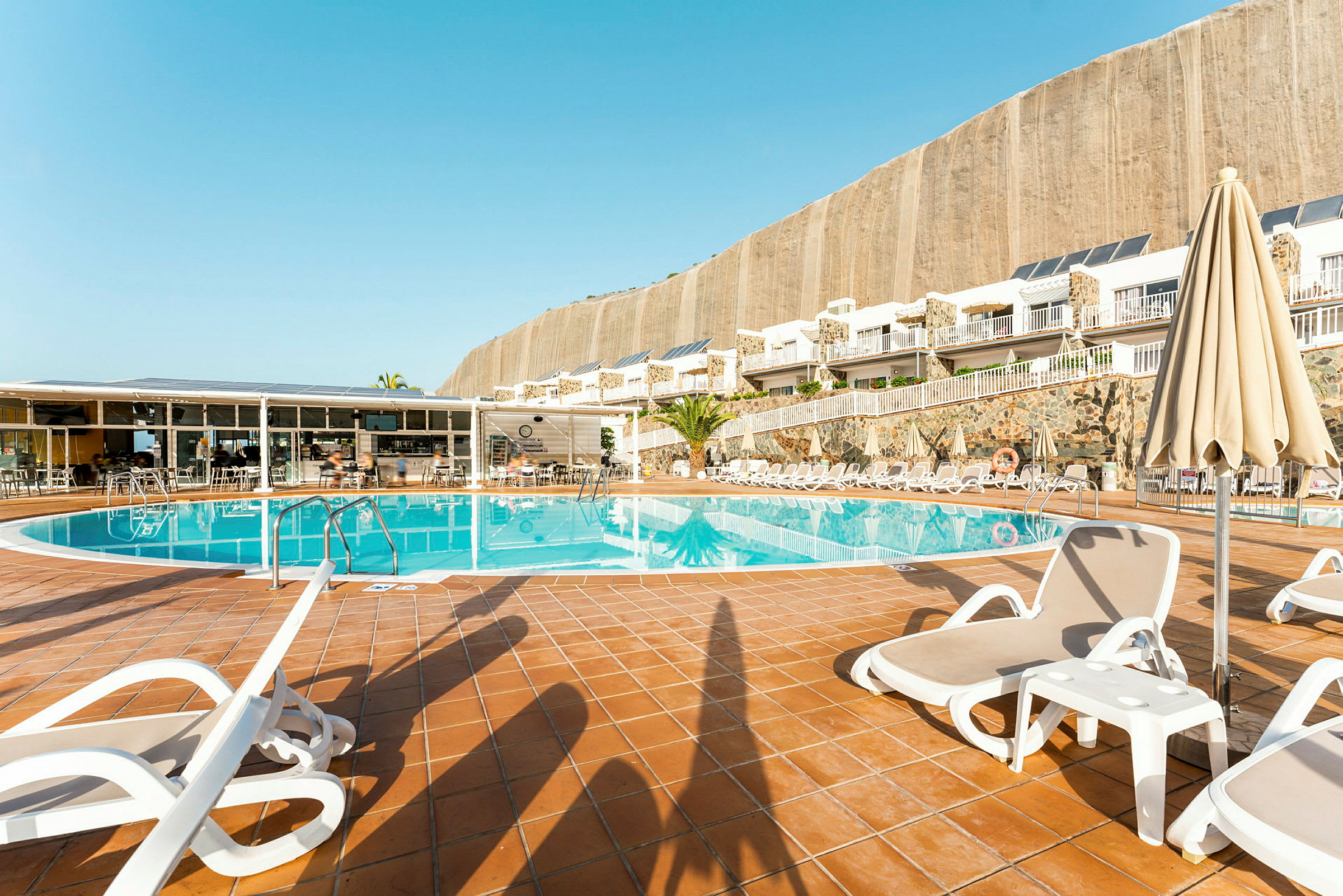 Udendørs pool med liggestole og parasoller ved en hotelbygning. (AI-genereret tekst)