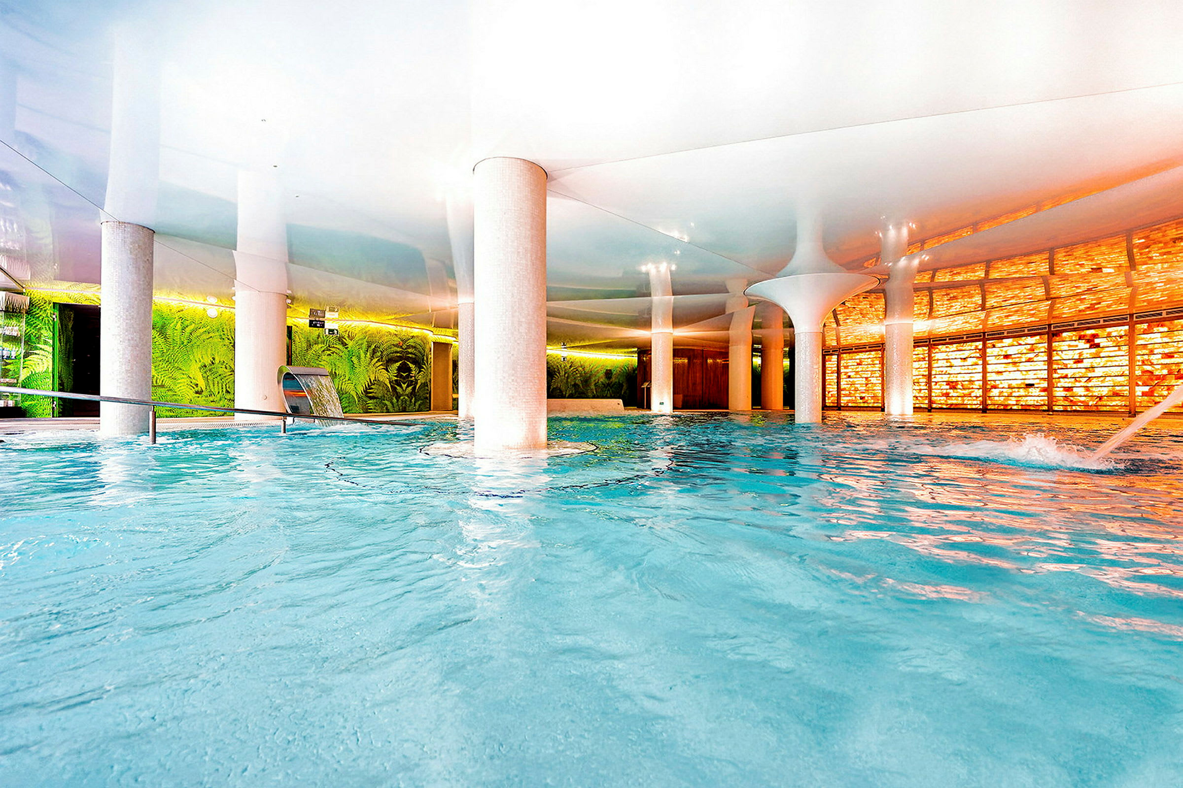 En indendørs swimmingpool med moderne design og detaljer som vægge med grønne planter og en oplyst panel. (AI-genereret tekst)