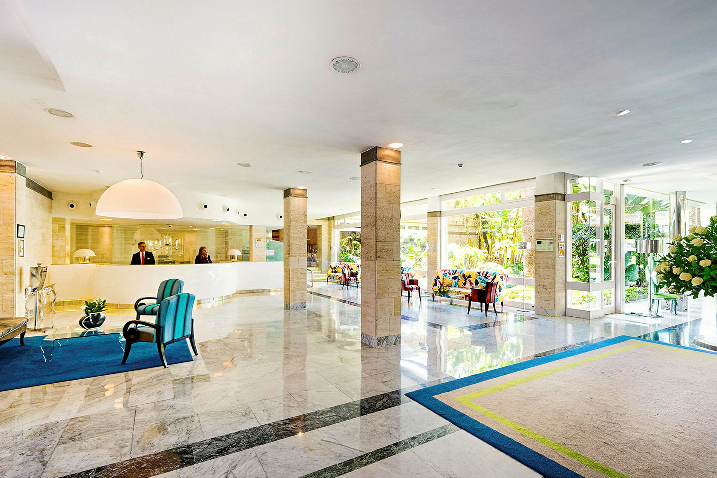 Lys hotellobby med reception, siddepladser og glasdøre. (AI-genereret tekst)