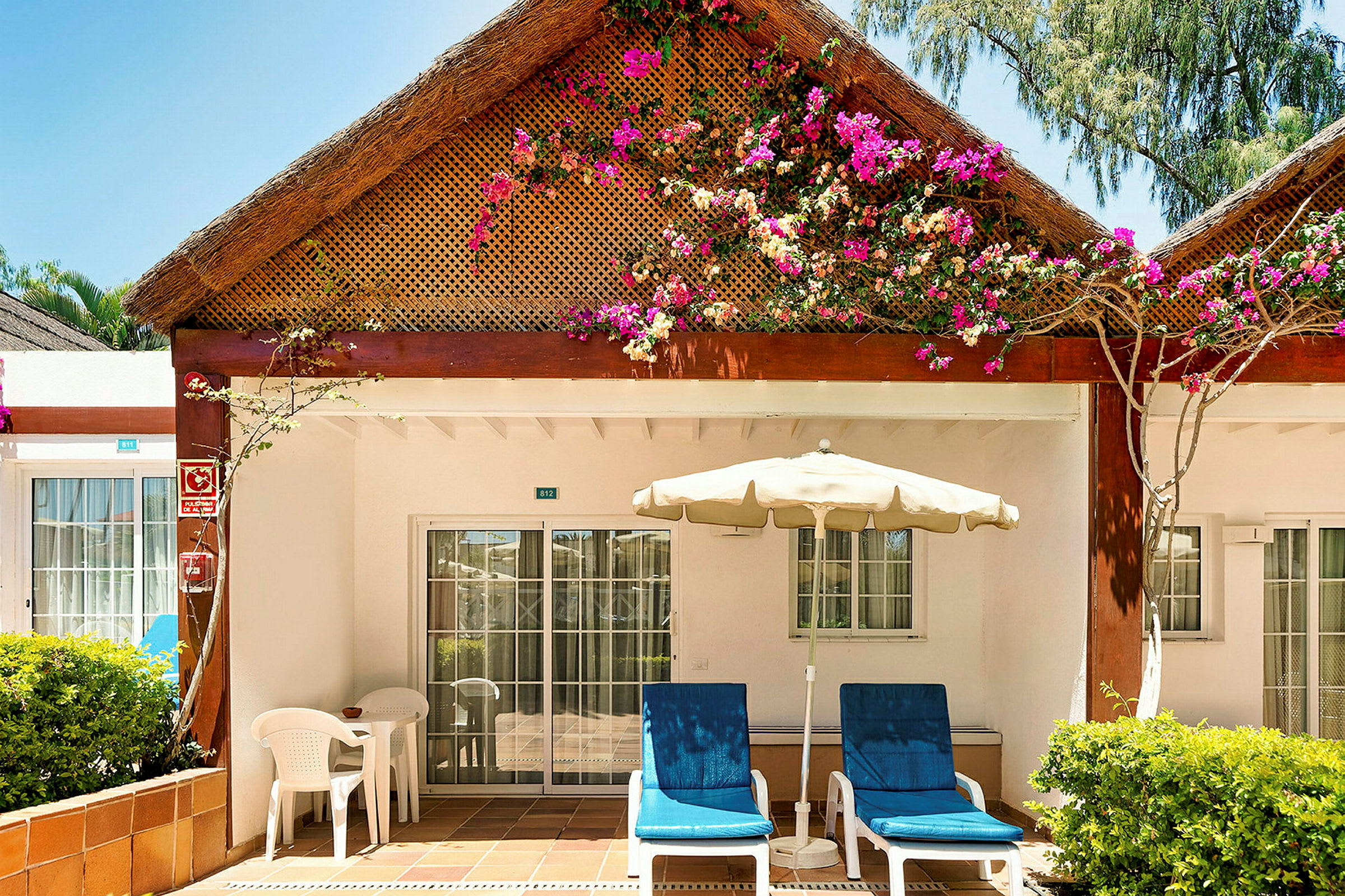 En terrasse ved en bungalow med blomster på taget. (AI-genereret tekst)