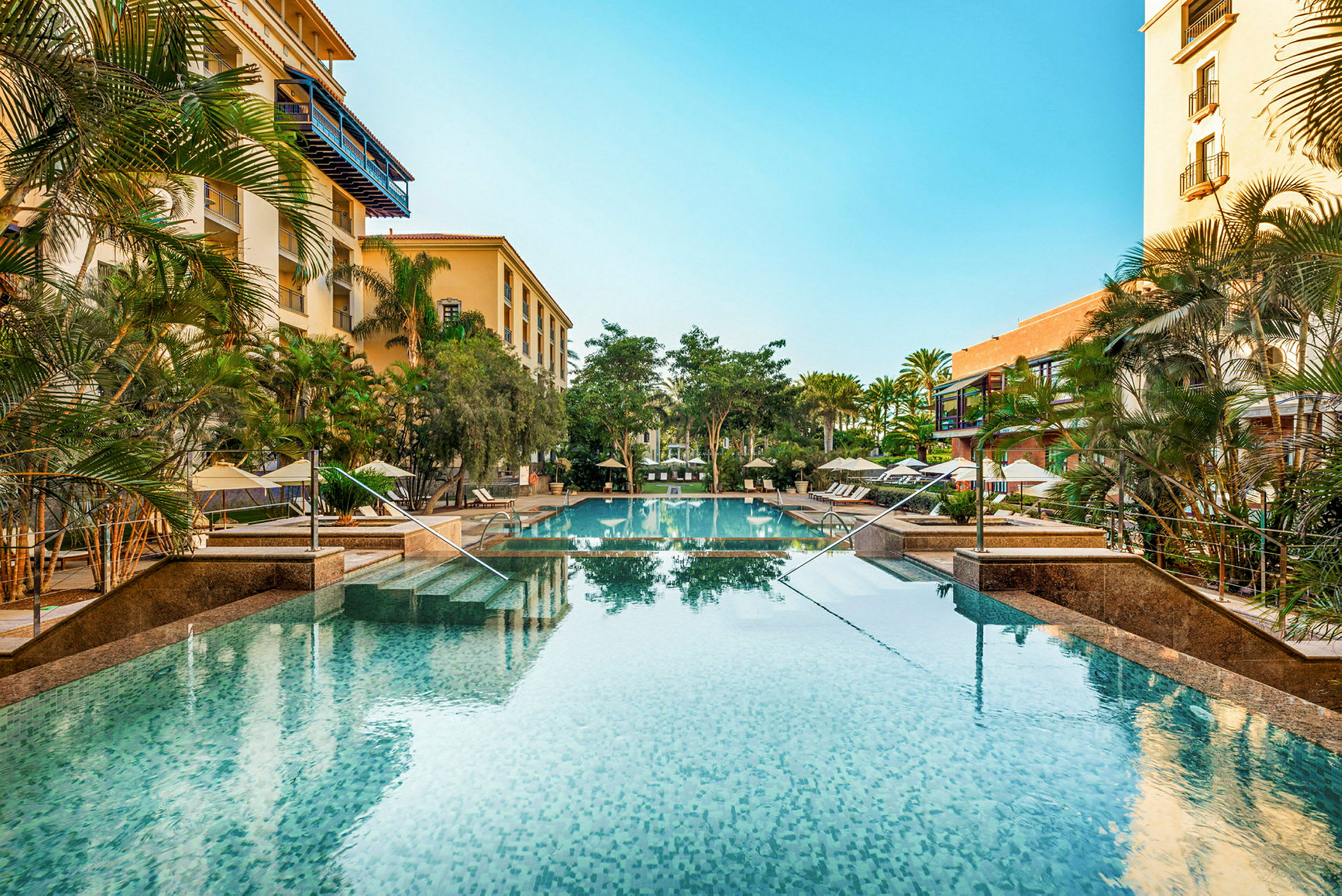 Hotelpool omgivet af grønne områder og bygninger. (AI-genereret tekst)