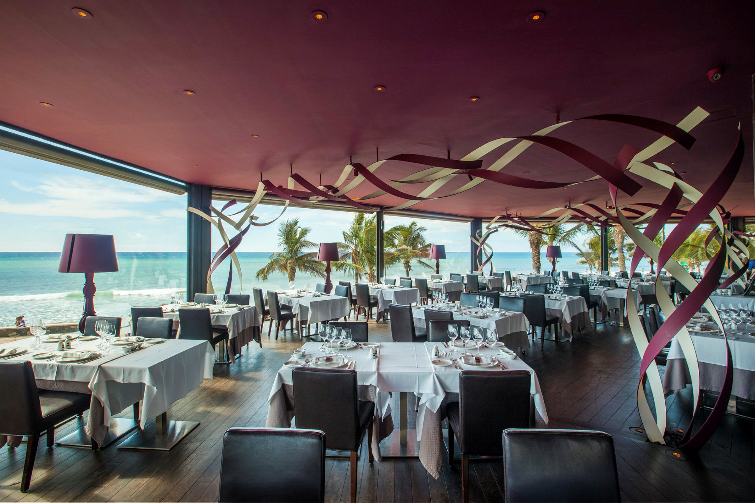 En restaurant med havudsigt, fyldt med pænt dækkede borde og moderne indretning. (AI-genereret tekst)