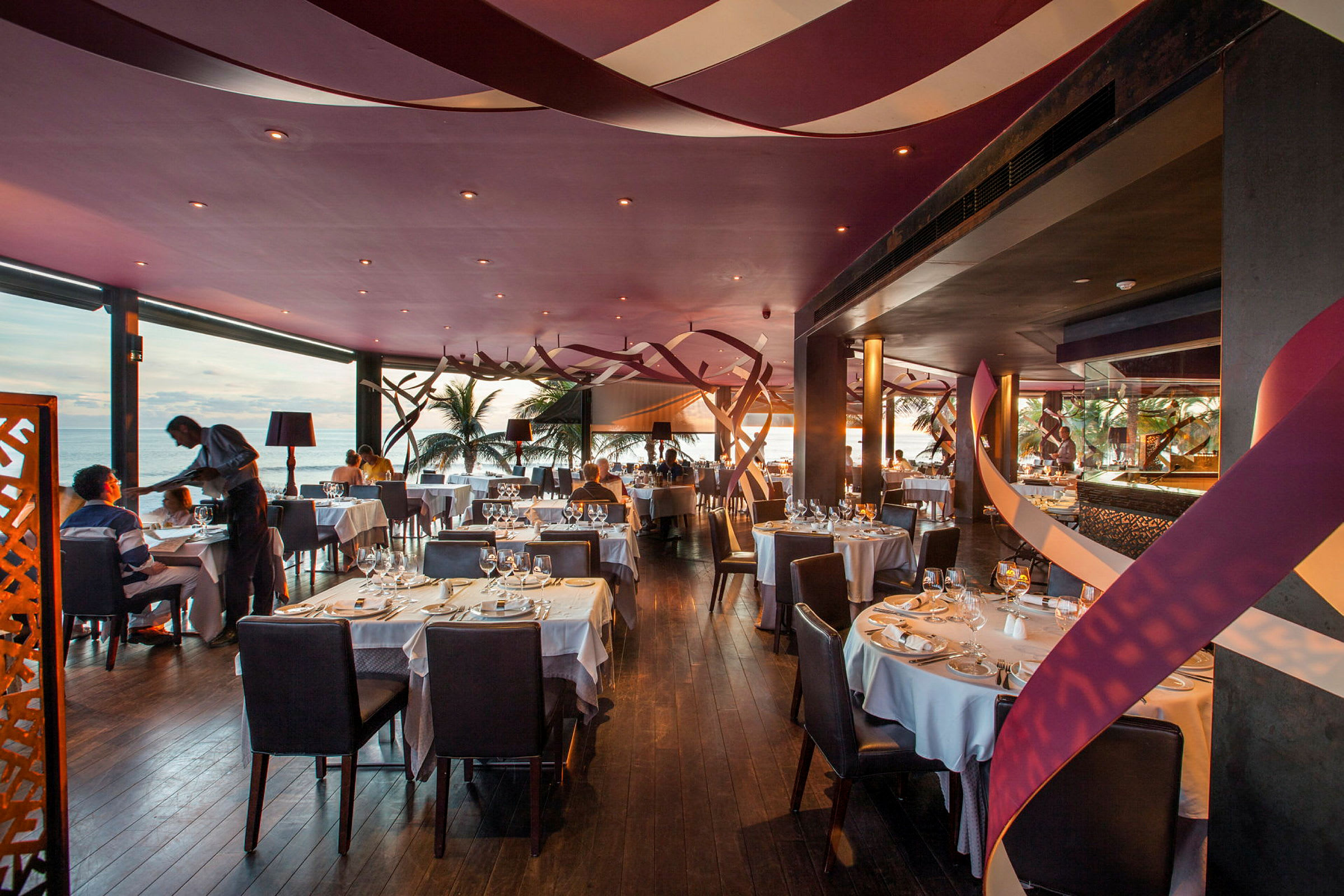 En elegant restaurant med opdækkede borde og havudsigt. (AI-genereret tekst)