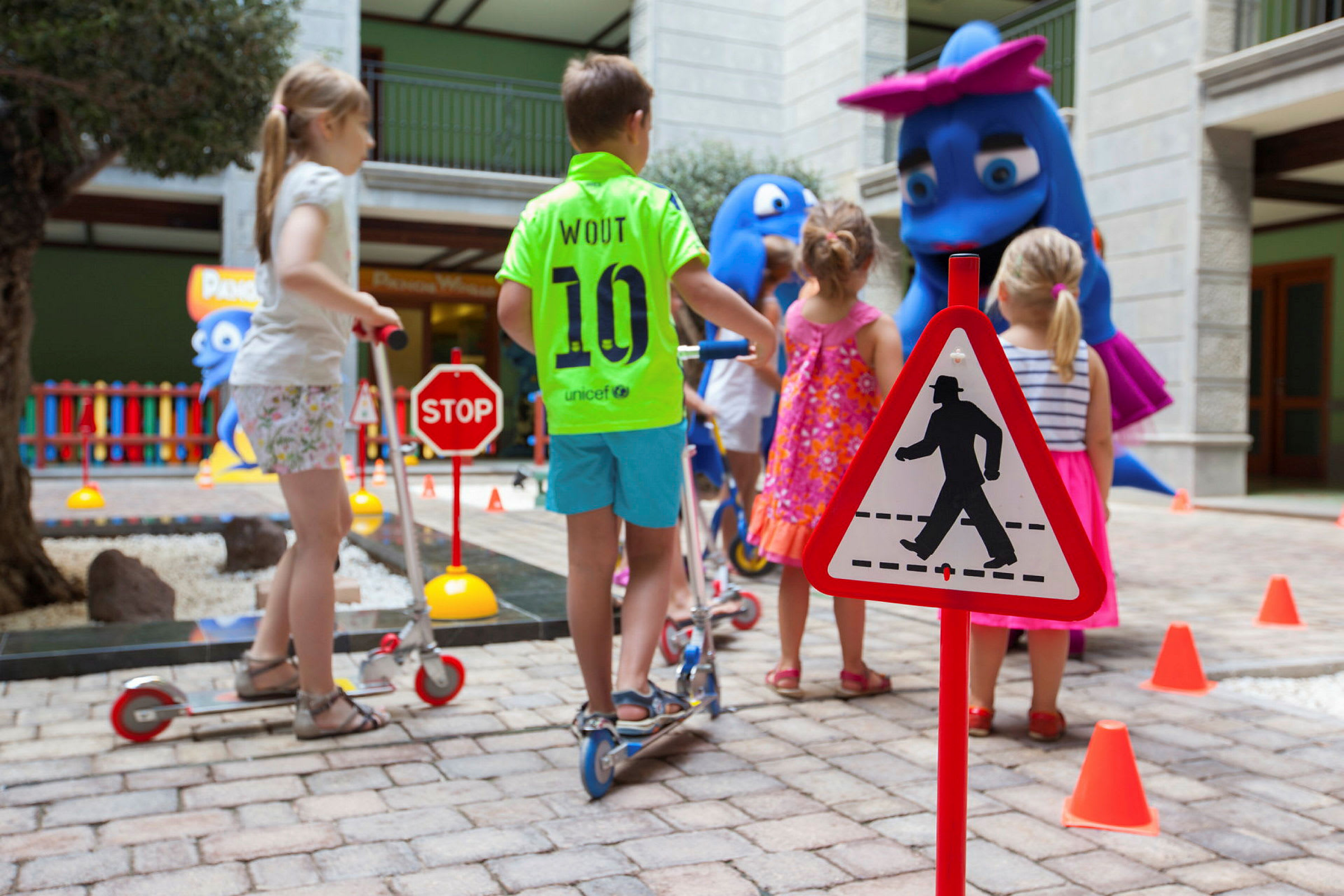 Børn leger på en bane indendørs med trafikskilte og figurer. (AI-genereret tekst)