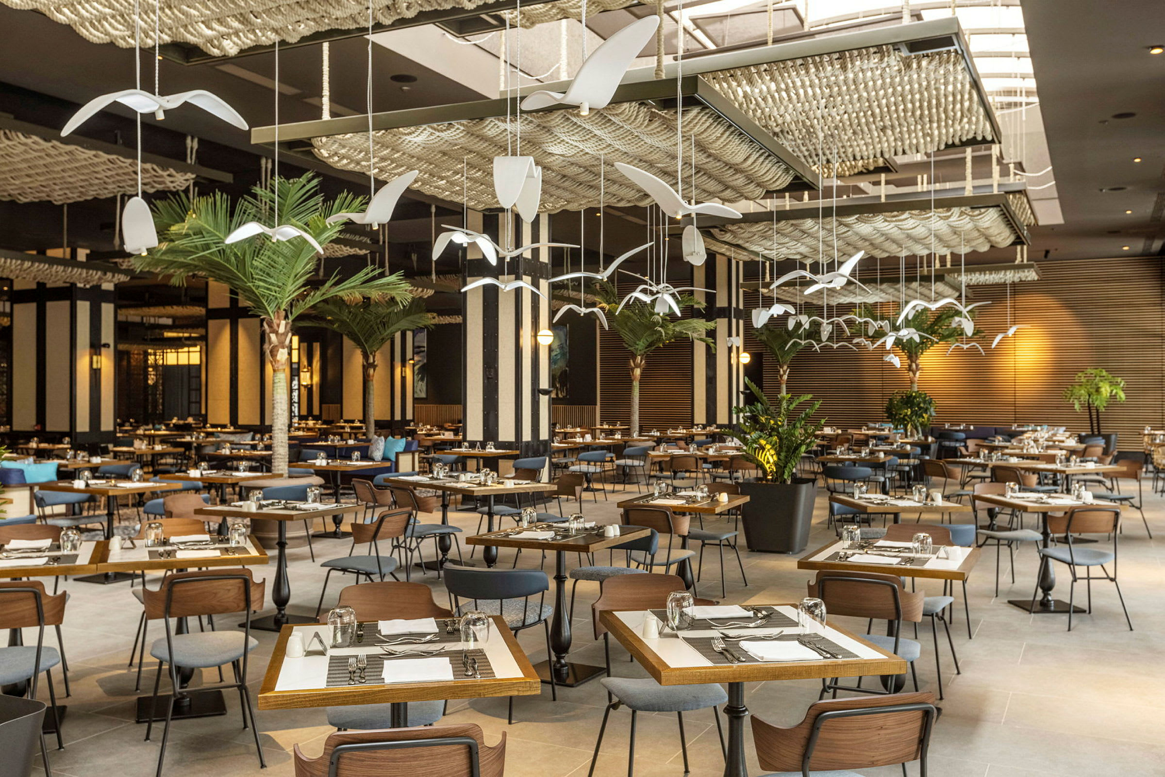 Restaurant med mange borde og stole, dekoreret med kunstneriske hængende elementer og beplantning. (AI-genereret tekst)
