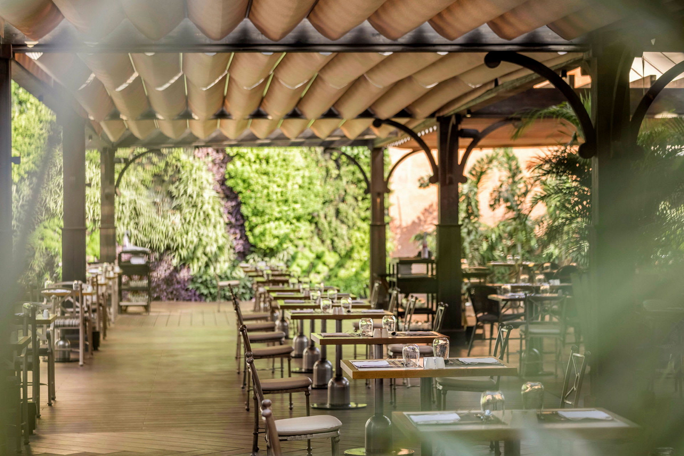 En terrasse-restaurant med træborde og stole, dekoreret med grønne planter. (AI-genereret tekst)