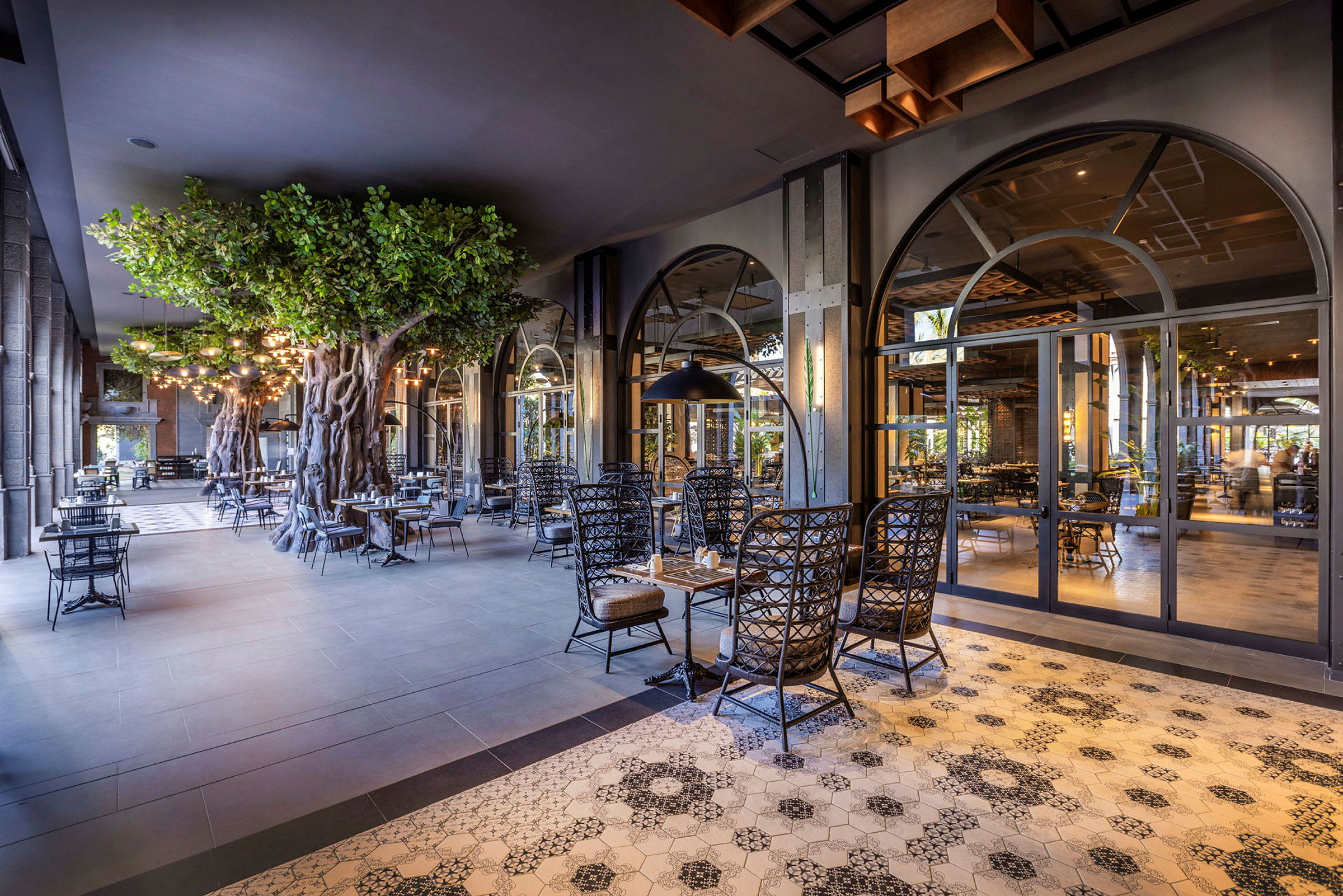 Et elegant restaurantområde med dekorative flisegulve, oplyste loftslamper og kunstige træer, der skaber en stemningsfuld atmosfære. (AI-genereret tekst)