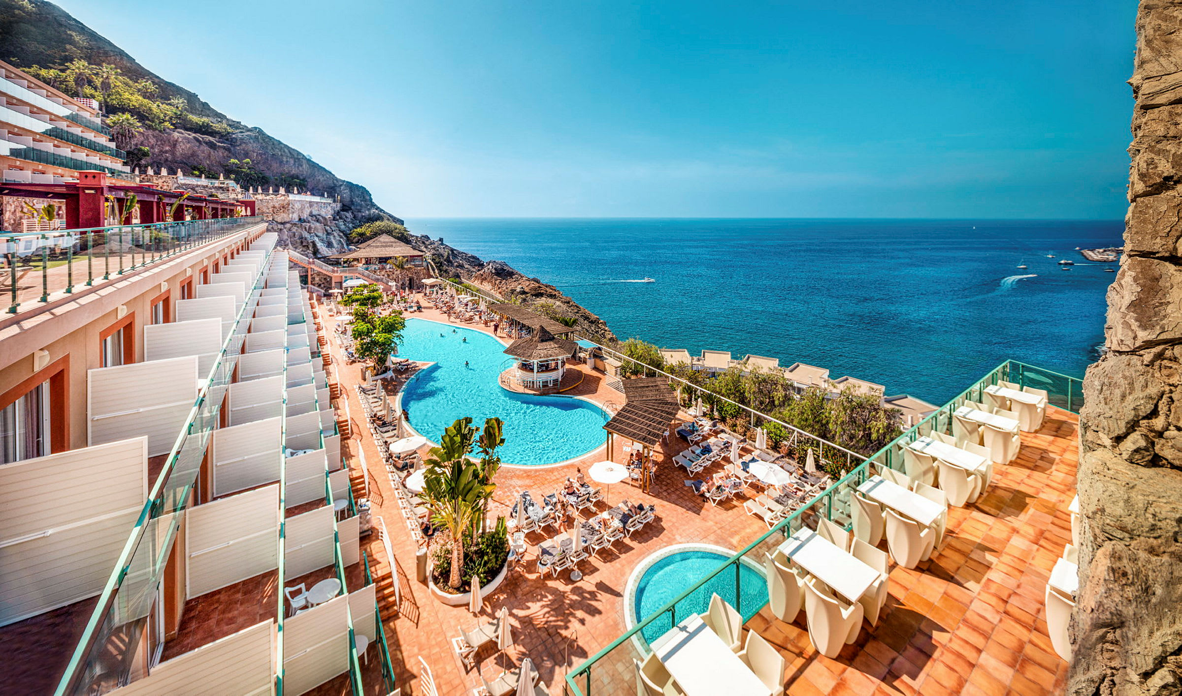 Udsigt over hotelområde med pools og havet. (AI-genereret tekst)