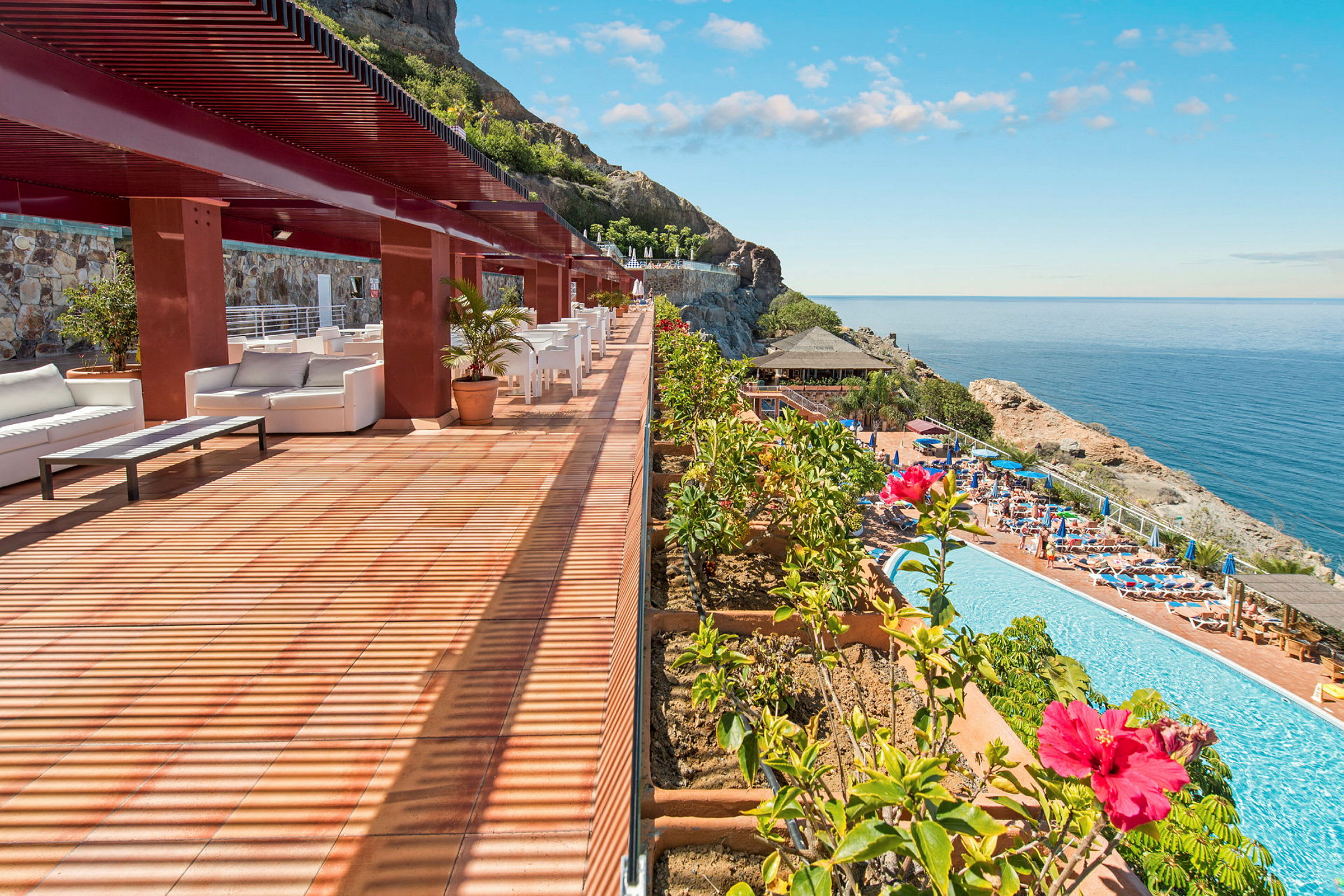 En terrasse med siddepladser og udsigt over en pool og havet. (AI-genereret tekst)