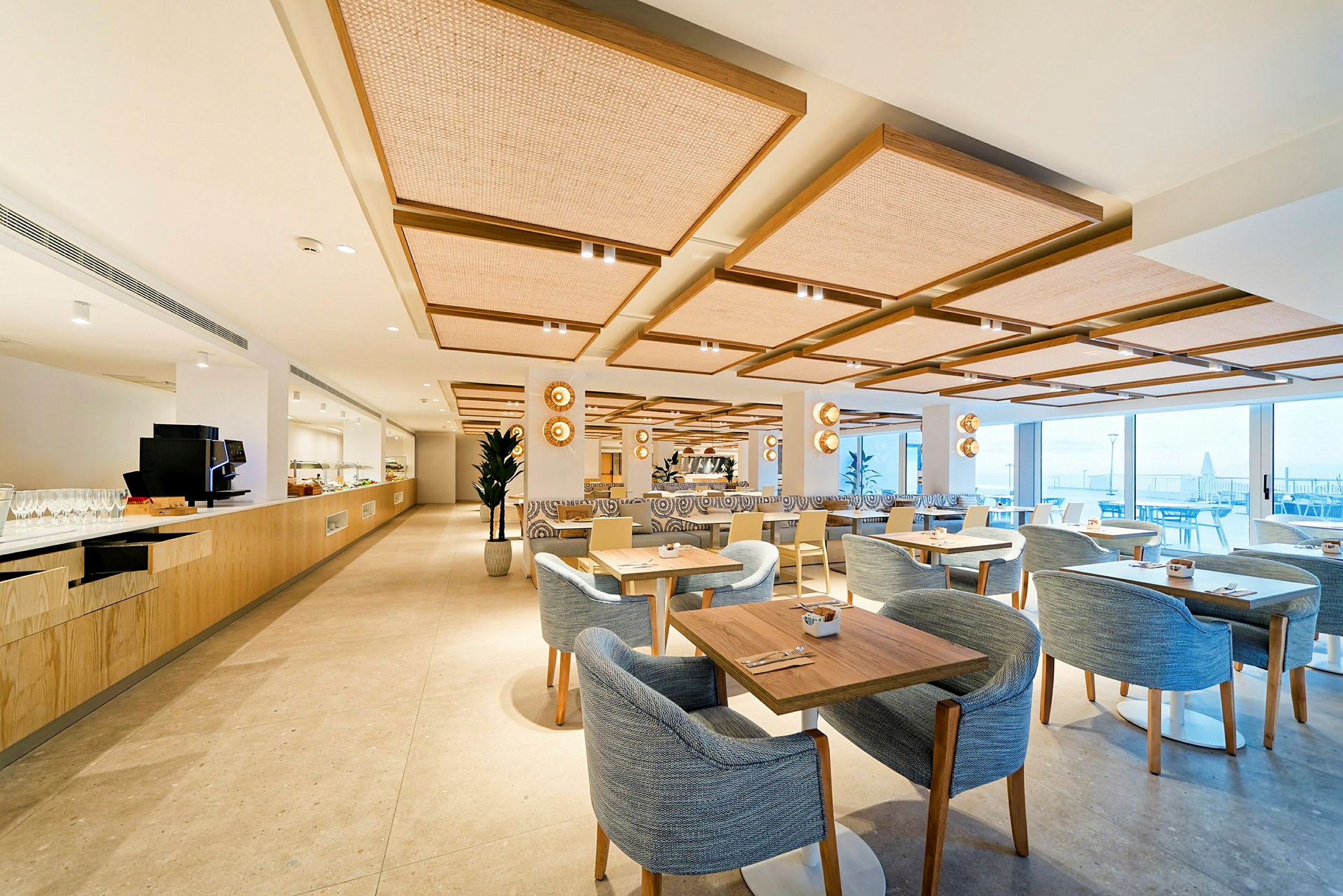 En moderne restaurant med lys indretning, borde og stole samt store vinduer med udsigt. (AI-genereret tekst)