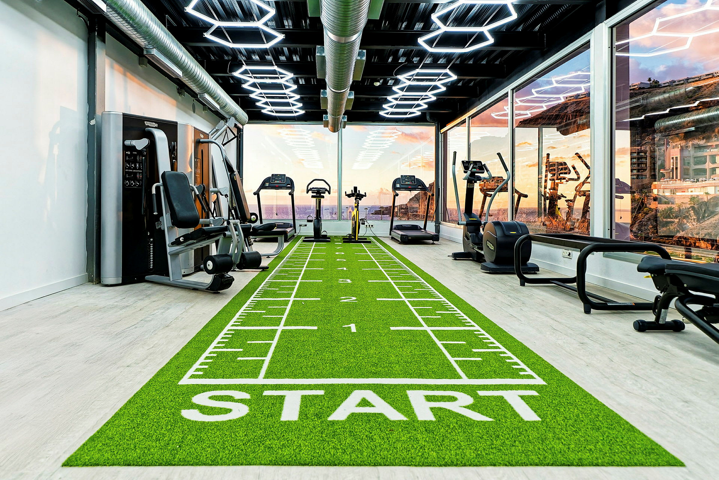 Billede af et fitnesscenter med træningsmaskiner og en løbebane markeret med en startlinje. (AI-genereret tekst)