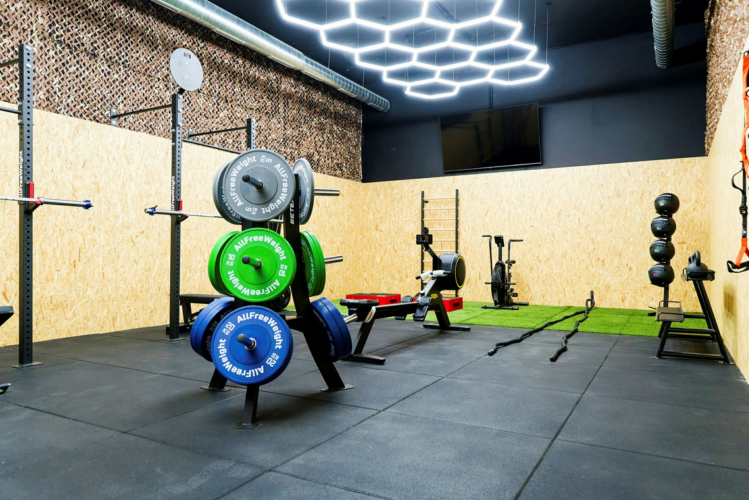 Træningsudstyr i et fitnessrum, inklusive vægtskiver, træningsmaskiner og en kunstgræsmåtte. (AI-genereret tekst)