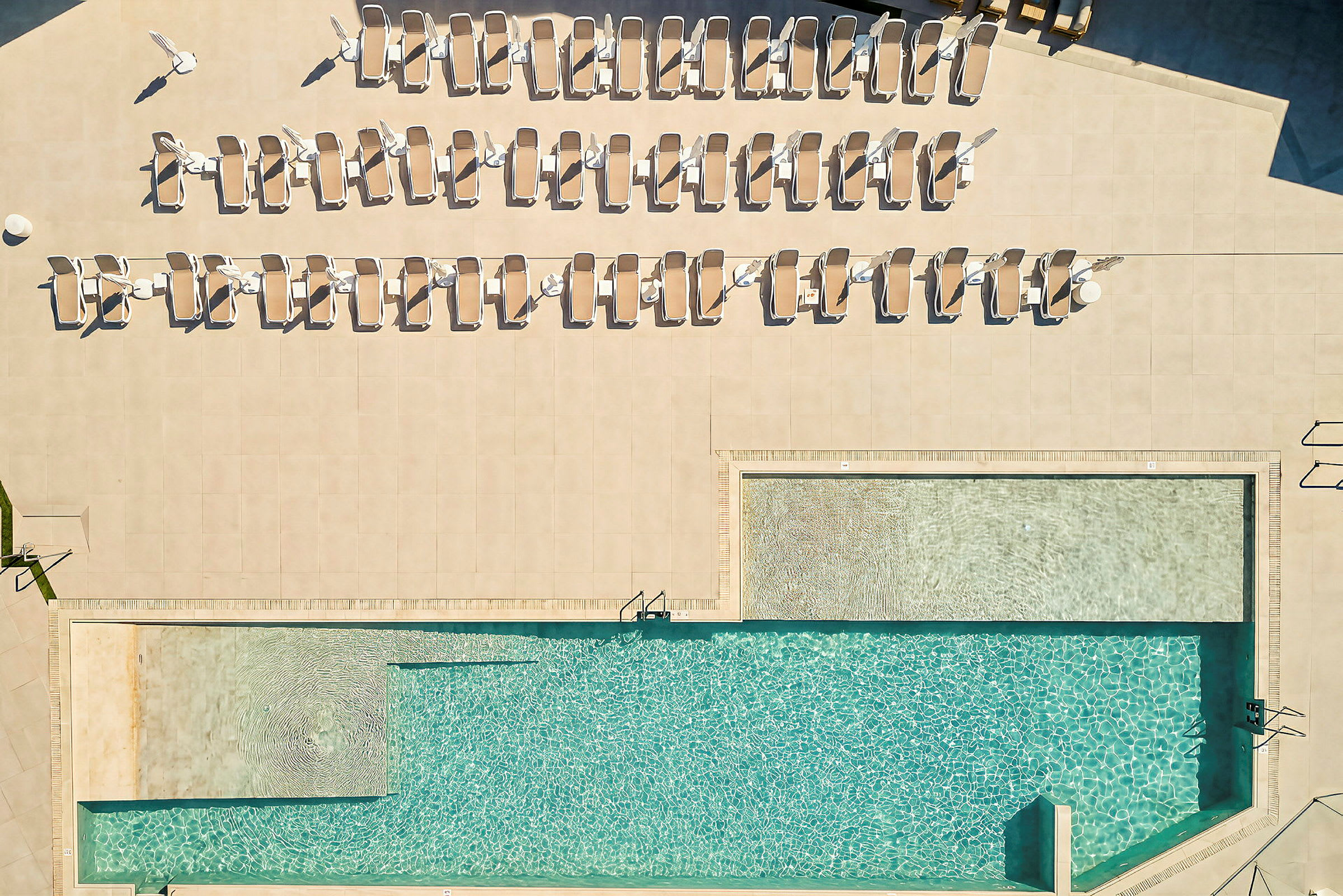 Udsigt ovenfra af en pool med liggestole omkring. (AI-genereret tekst)
