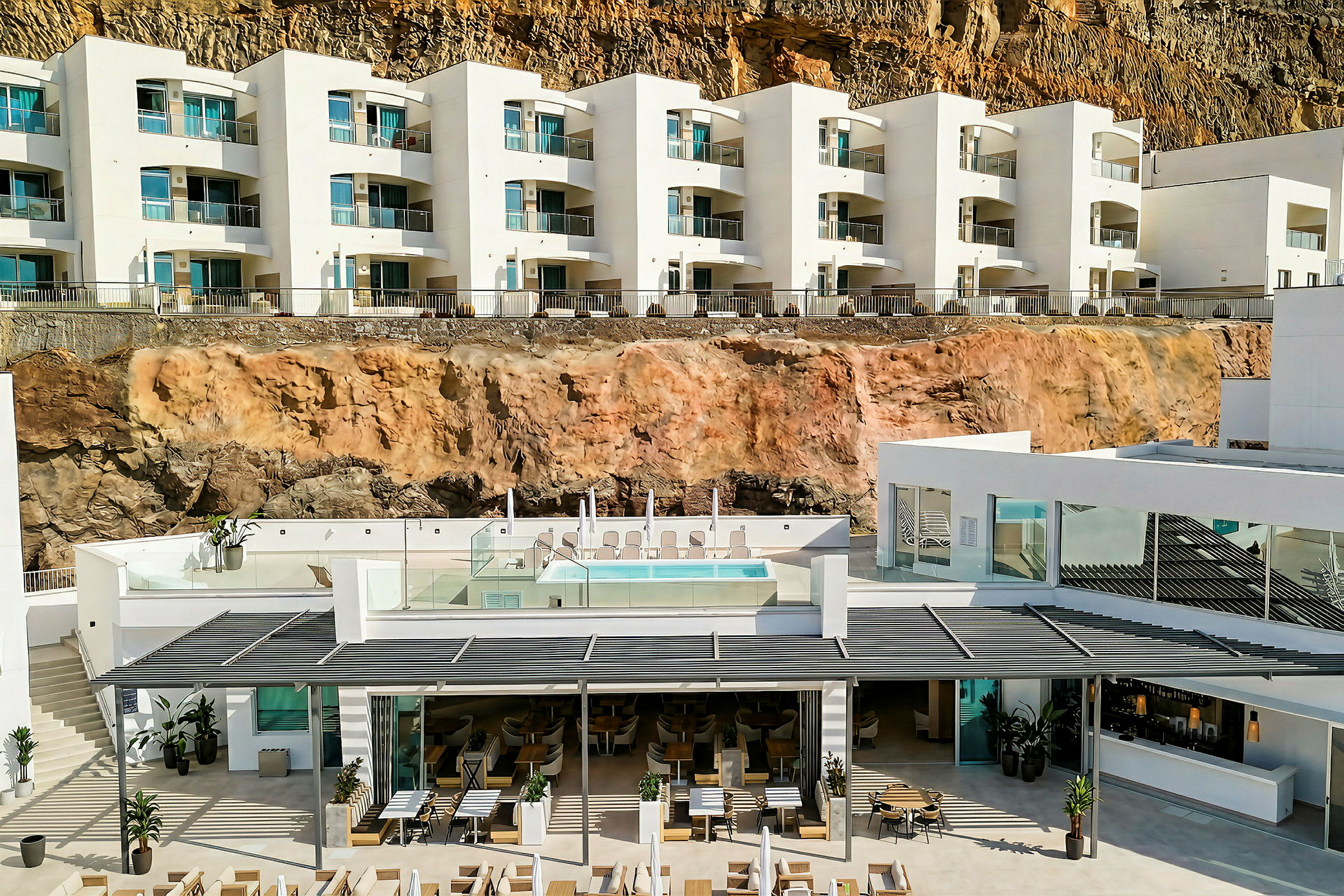 Et moderne hotel med hvide facader bygget ved en klippe. På den midterste etage ses en pool og solsenge. (AI-genereret tekst)