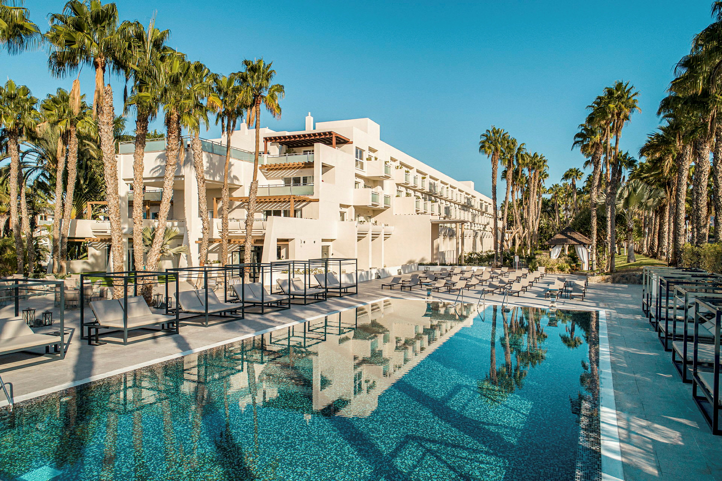 Moderne hotelbygning med pool og omkringliggende palmer. (AI-genereret tekst)