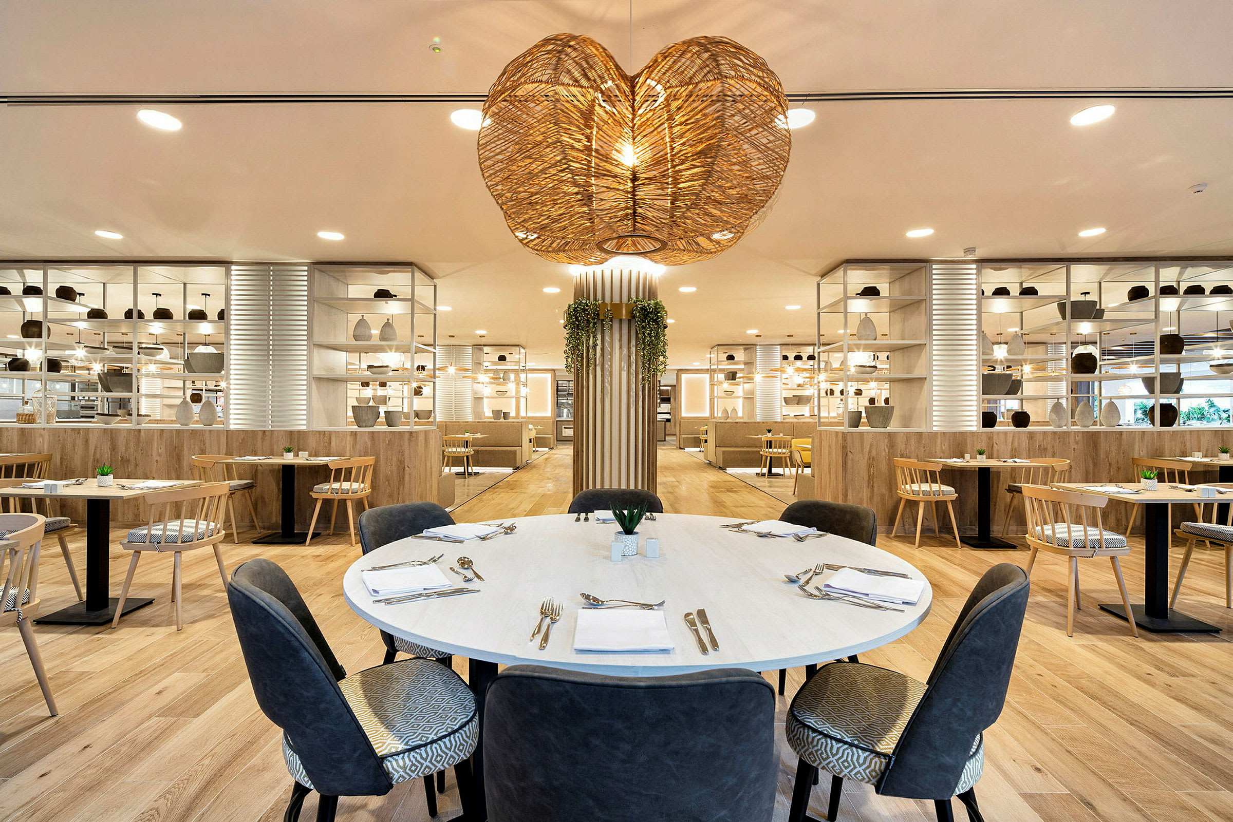 En moderne indrettet restaurantinteriør med et rundt bord i forgrunden, omgivet af siddepladser og dekorative hylder. (AI-genereret tekst)