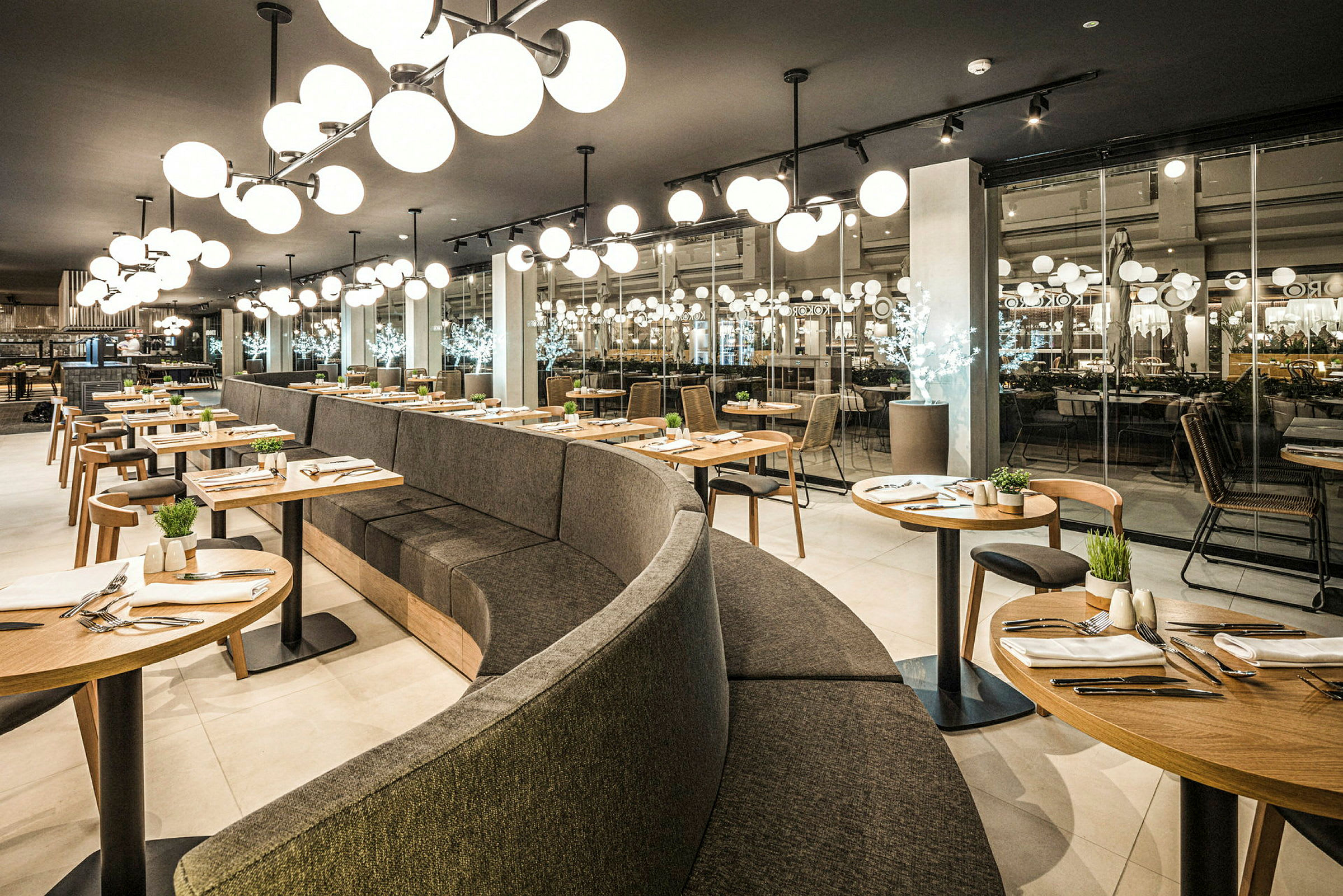 Moderne restaurantmiljø med buet siddeområde og runde borde, elegant indrettet. (AI-genereret tekst)