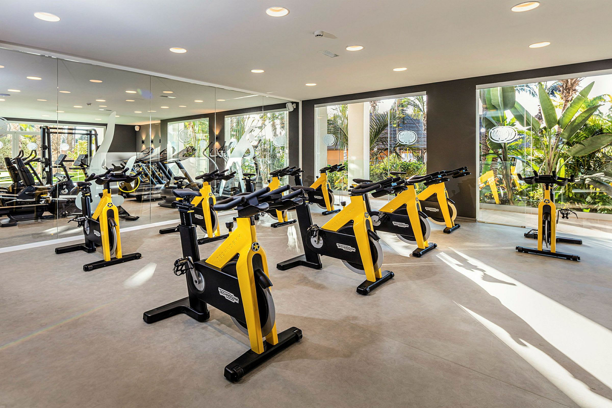 Et fitnesscenter med flere gule træningscykler placeret i et godt oplyst rum. (AI-genereret tekst)