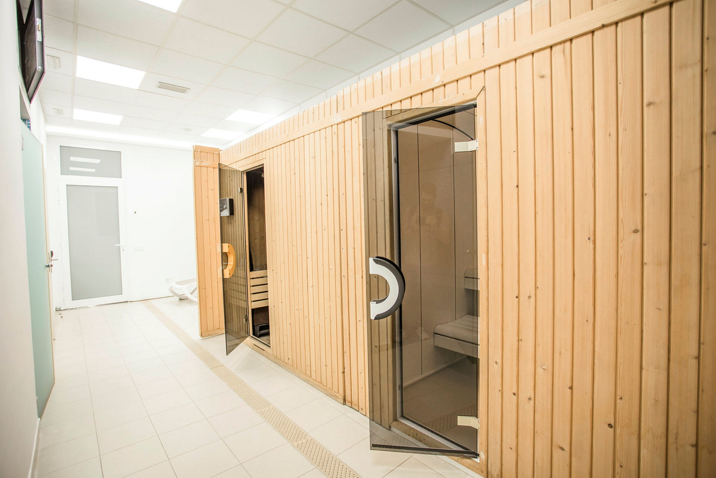 Billede af en sauna med træbeklædte vægge og glasdøre i et lyst indendørsmiljø. (AI-genereret tekst)