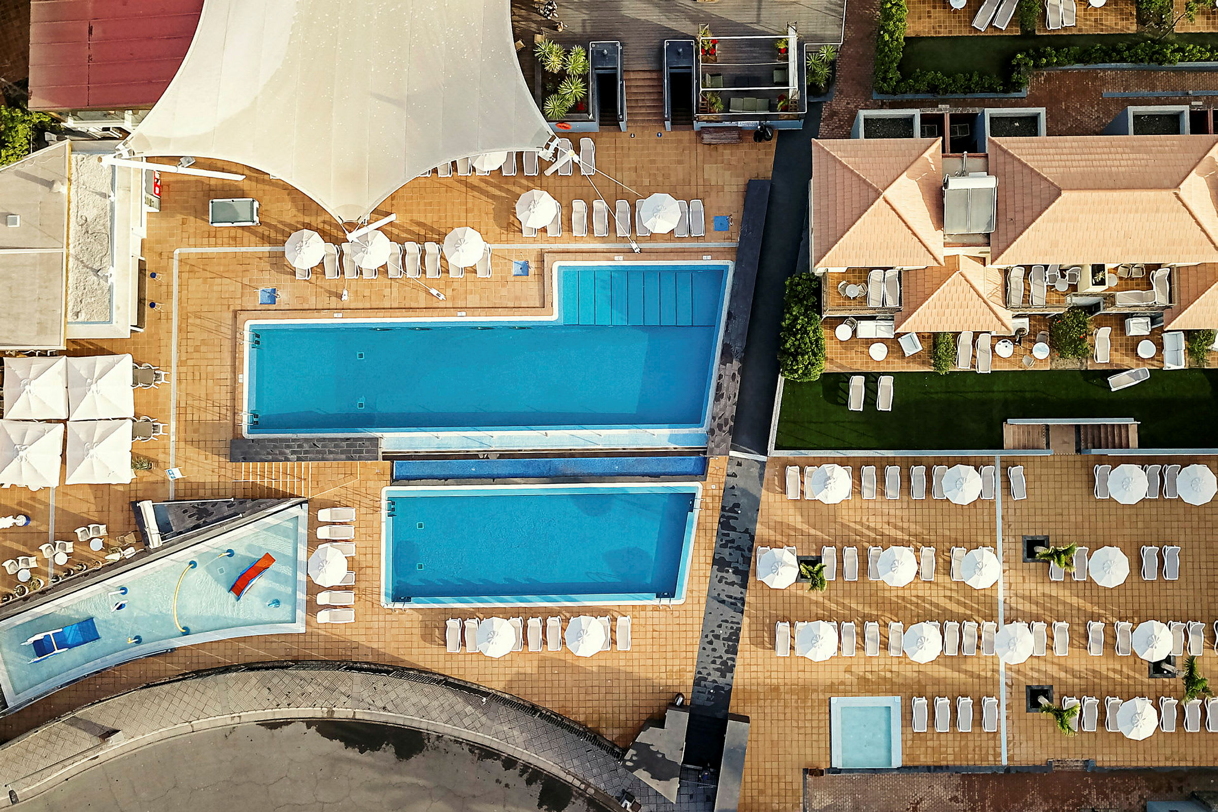 Luftfoto af hotelområde med pools og liggestole. (AI-genereret tekst)
