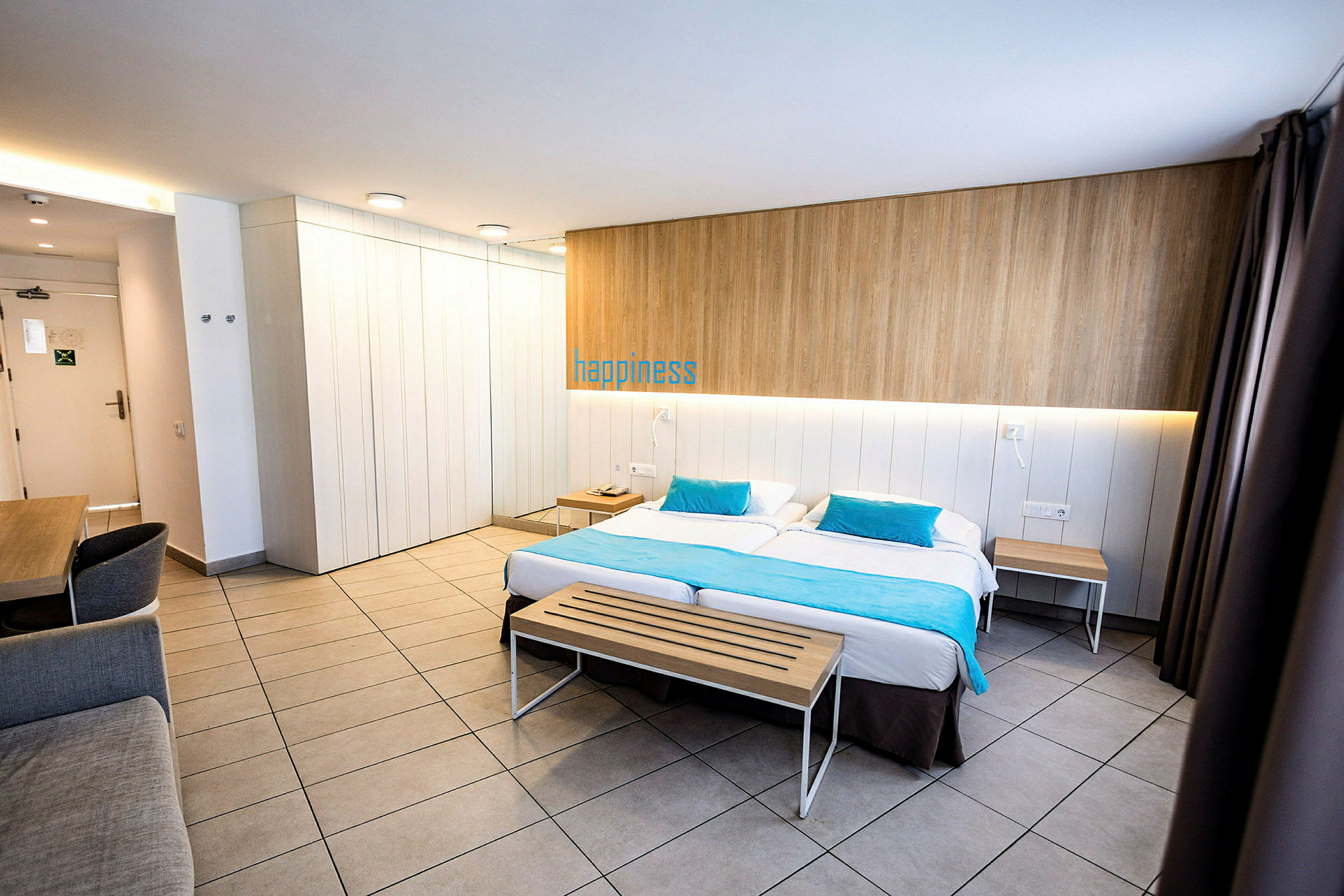 Et moderne hotelværelse med en dobbeltseng, en træbænk for enden og et skrivebord i hjørnet. (AI-genereret tekst)
