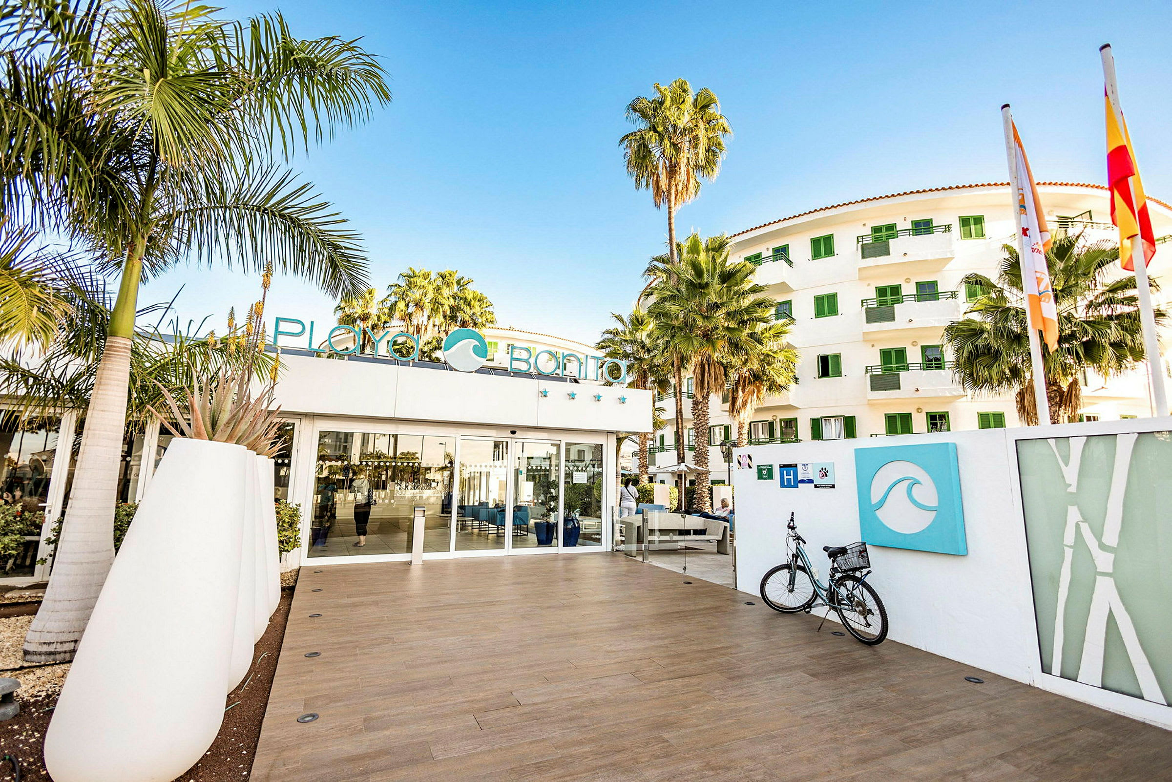 Indgang til hotel Playa Bonito med moderne plantekrukker, cykelparkering og frodige palmer. (AI-genereret tekst)