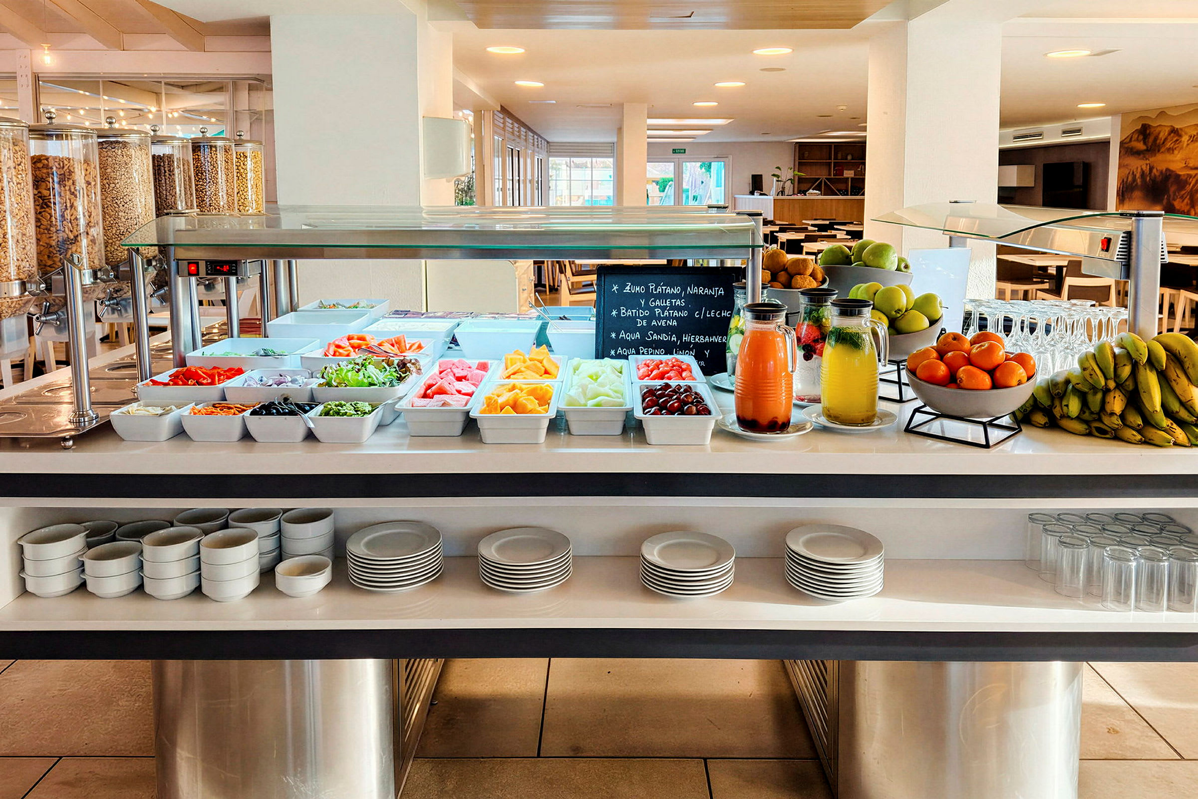 En buffet med tallerkener og glas samt frugt, juice og salat i skåle på et bord. (AI-genereret tekst)