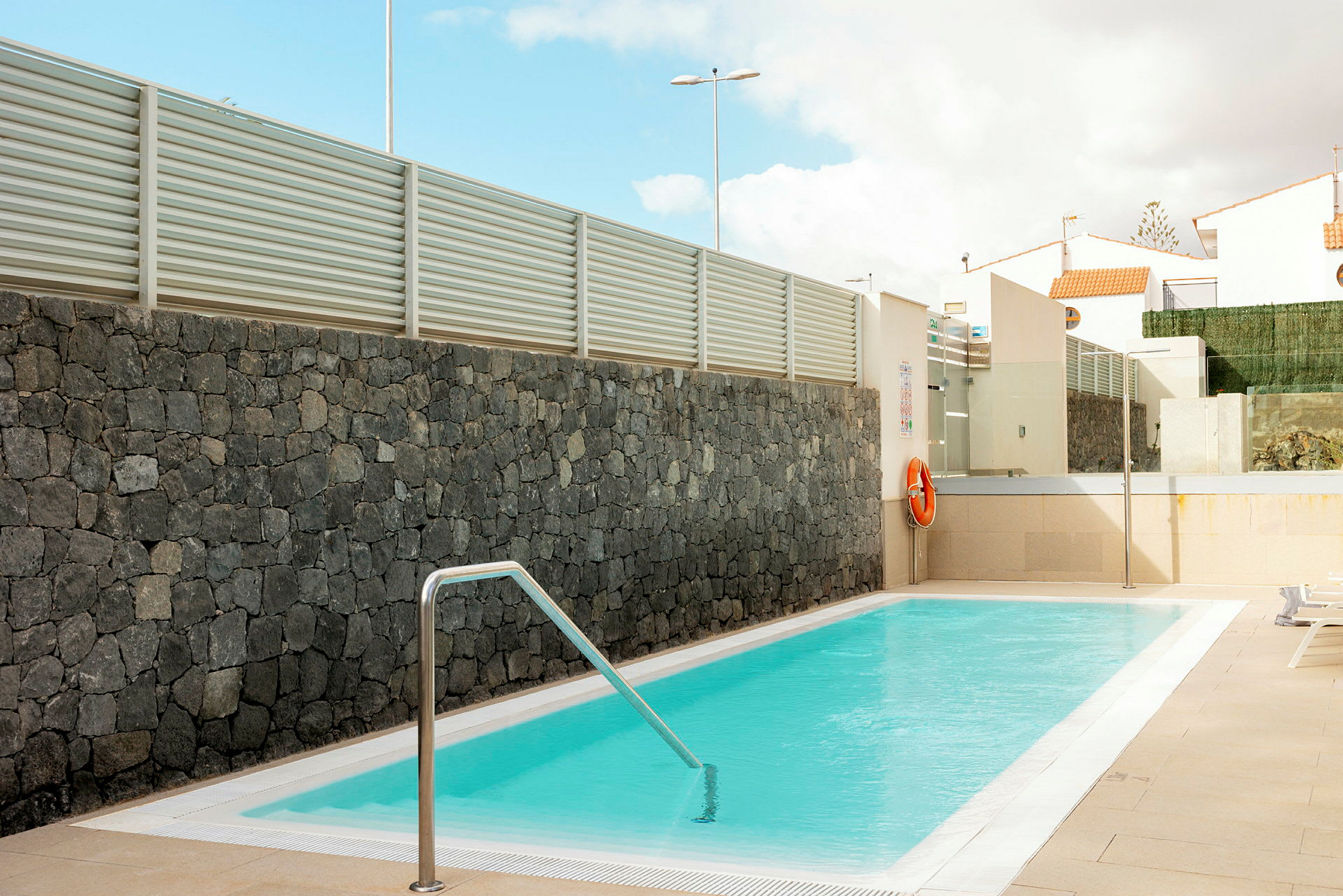 En udendørs pool med klart vand omgivet af stenmur og moderne arkitektur. (AI-genereret tekst)